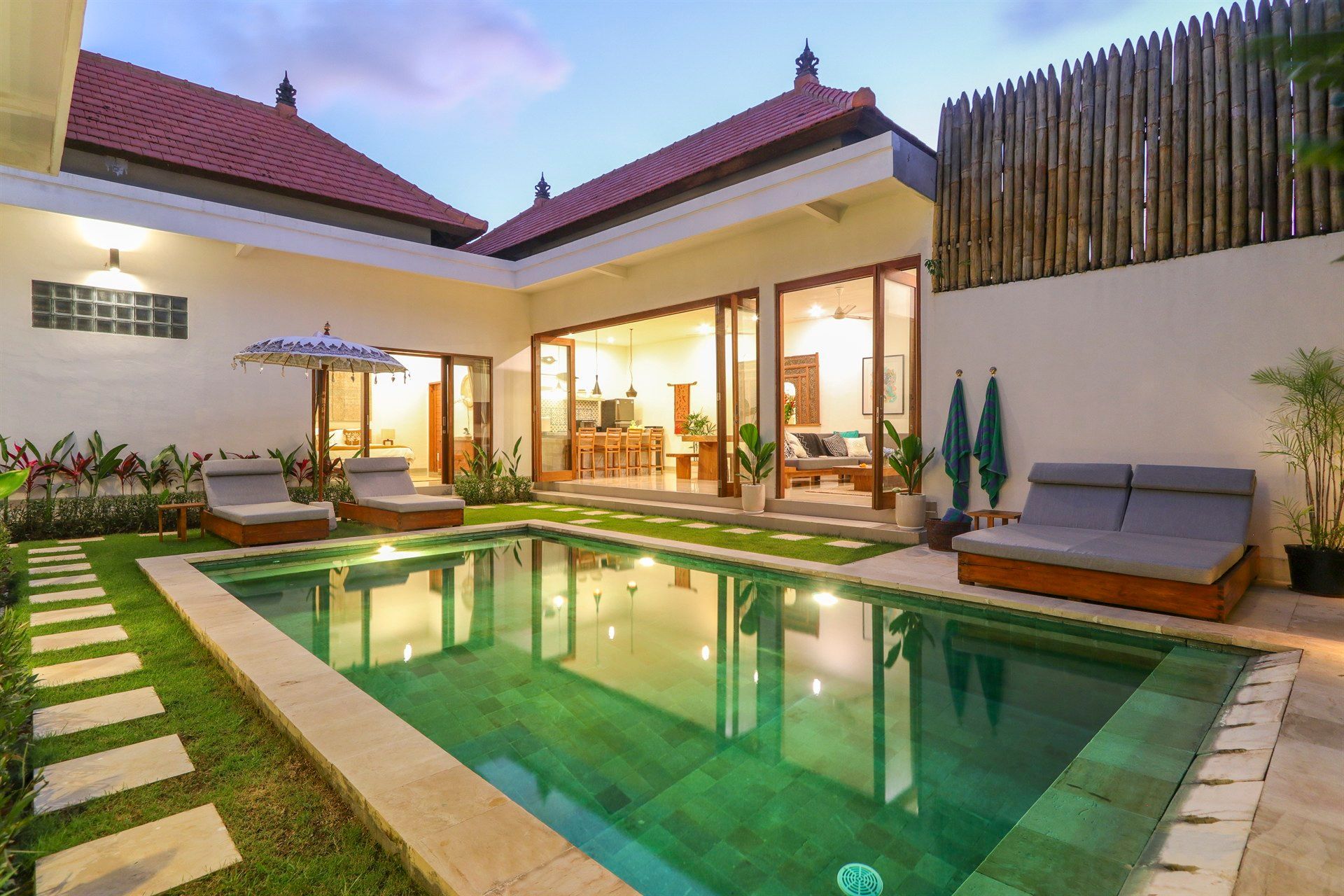 Poolside villa with pool, lounge chairs, and open-plan living area, at dusk.