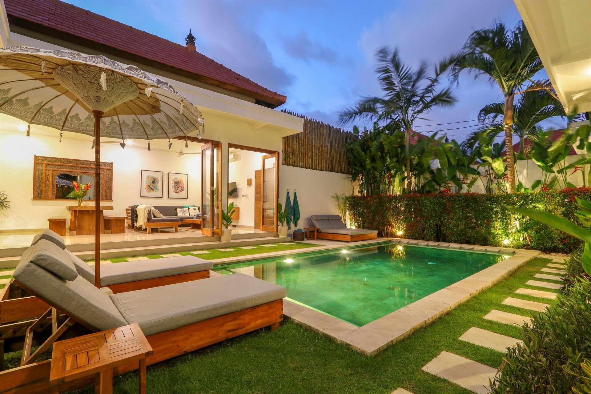 Lounge chairs by a pool, open-air living space, tropical setting, dusk.