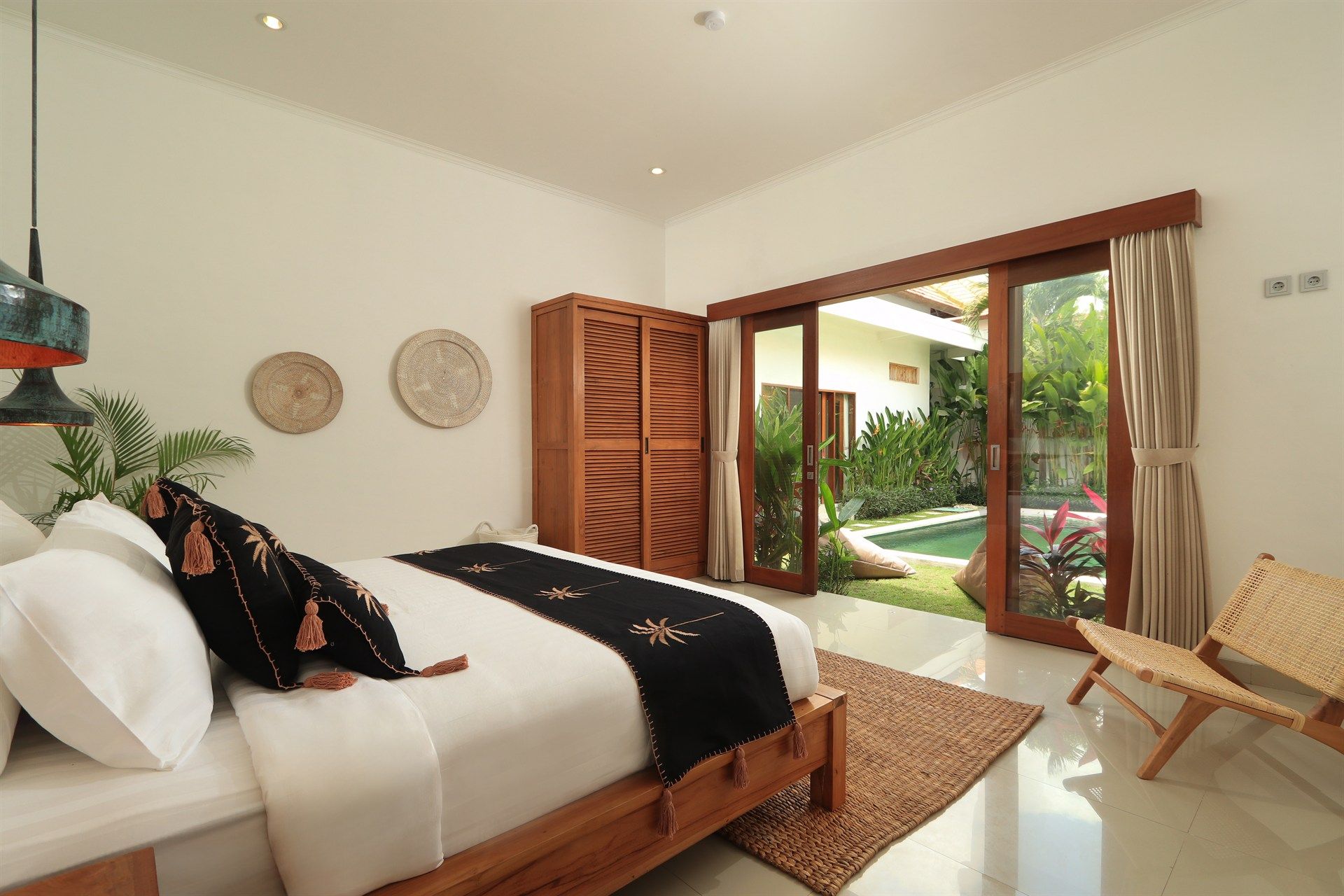 Bedroom with wooden bed, wardrobe, sliding door to yard, and woven chair.