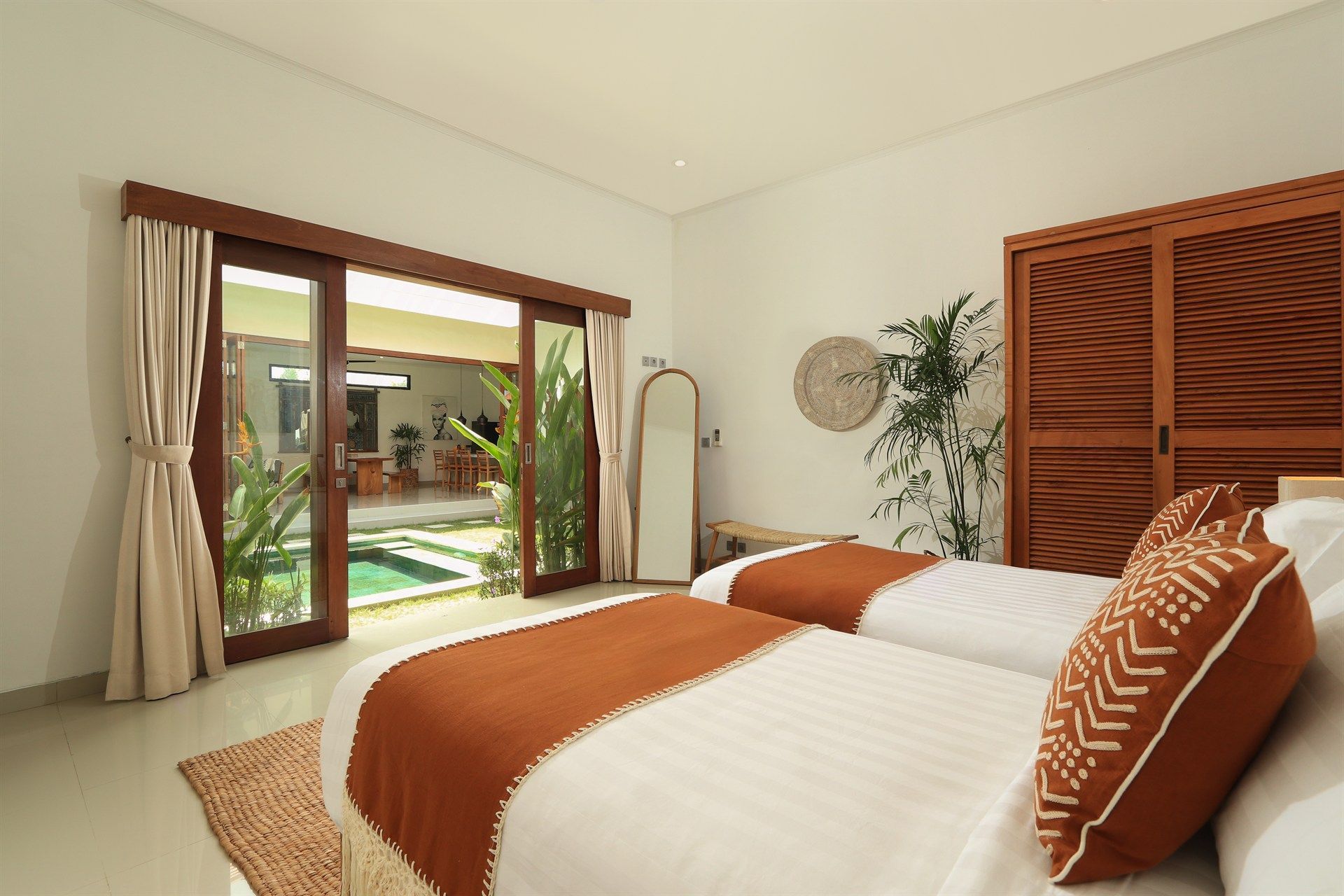 Bedroom with two twin beds, large sliding doors to pool area, neutral tones, and decorative pillows.