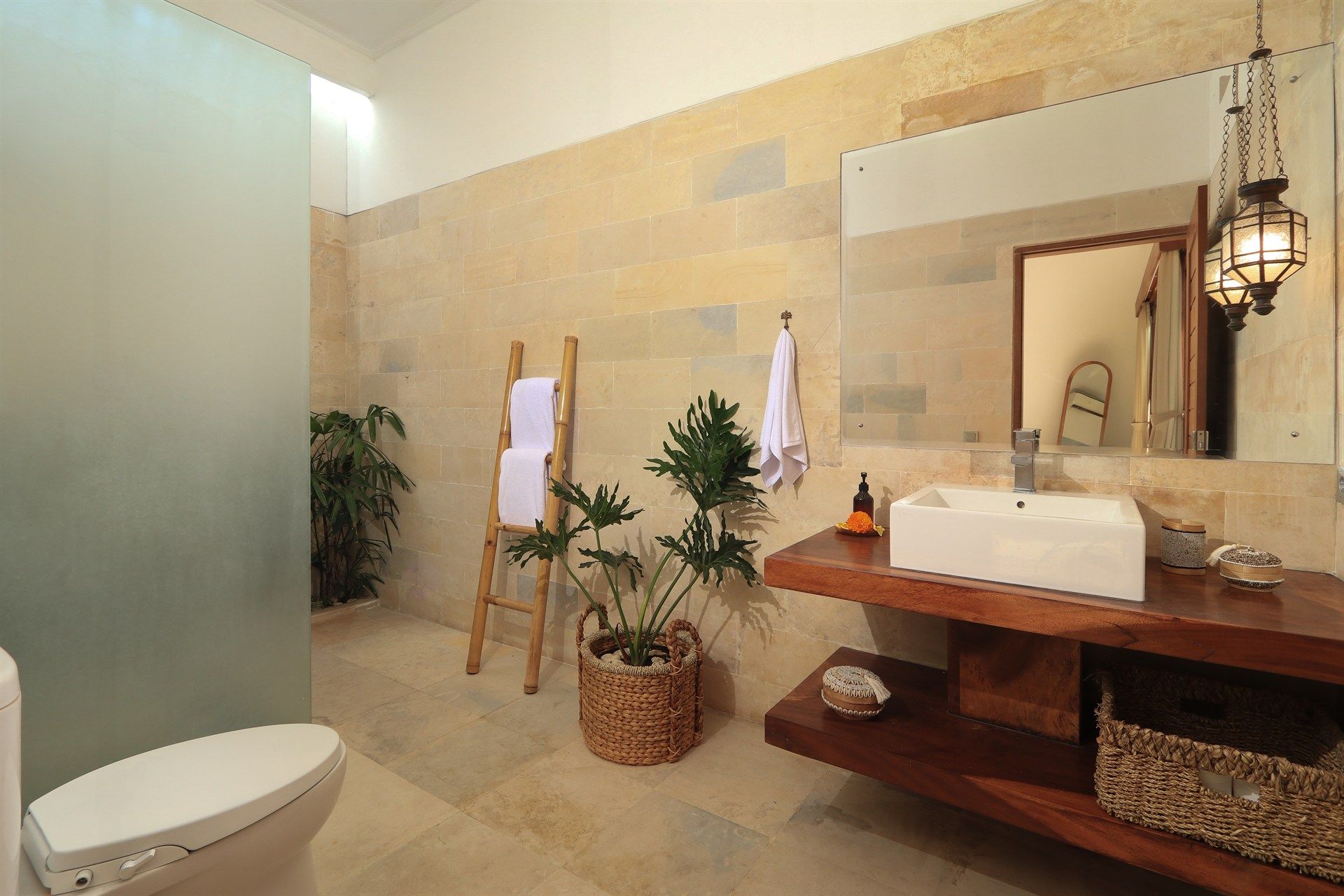 Spa-like bathroom with stone walls, wooden vanity, a large mirror, and plants.