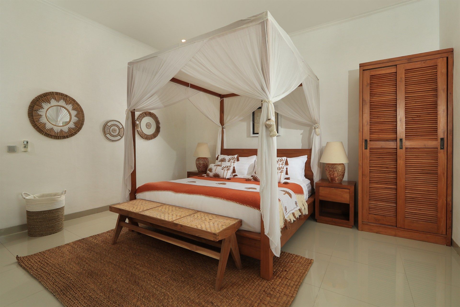 Bedroom with canopy bed, wooden furniture, woven rug, and wall decorations.