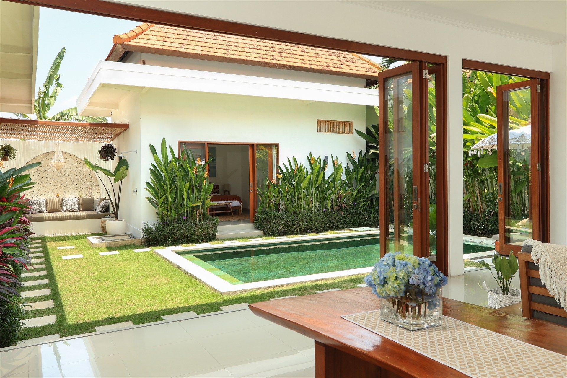 Open doors lead to a tropical home with a pool and lush garden.