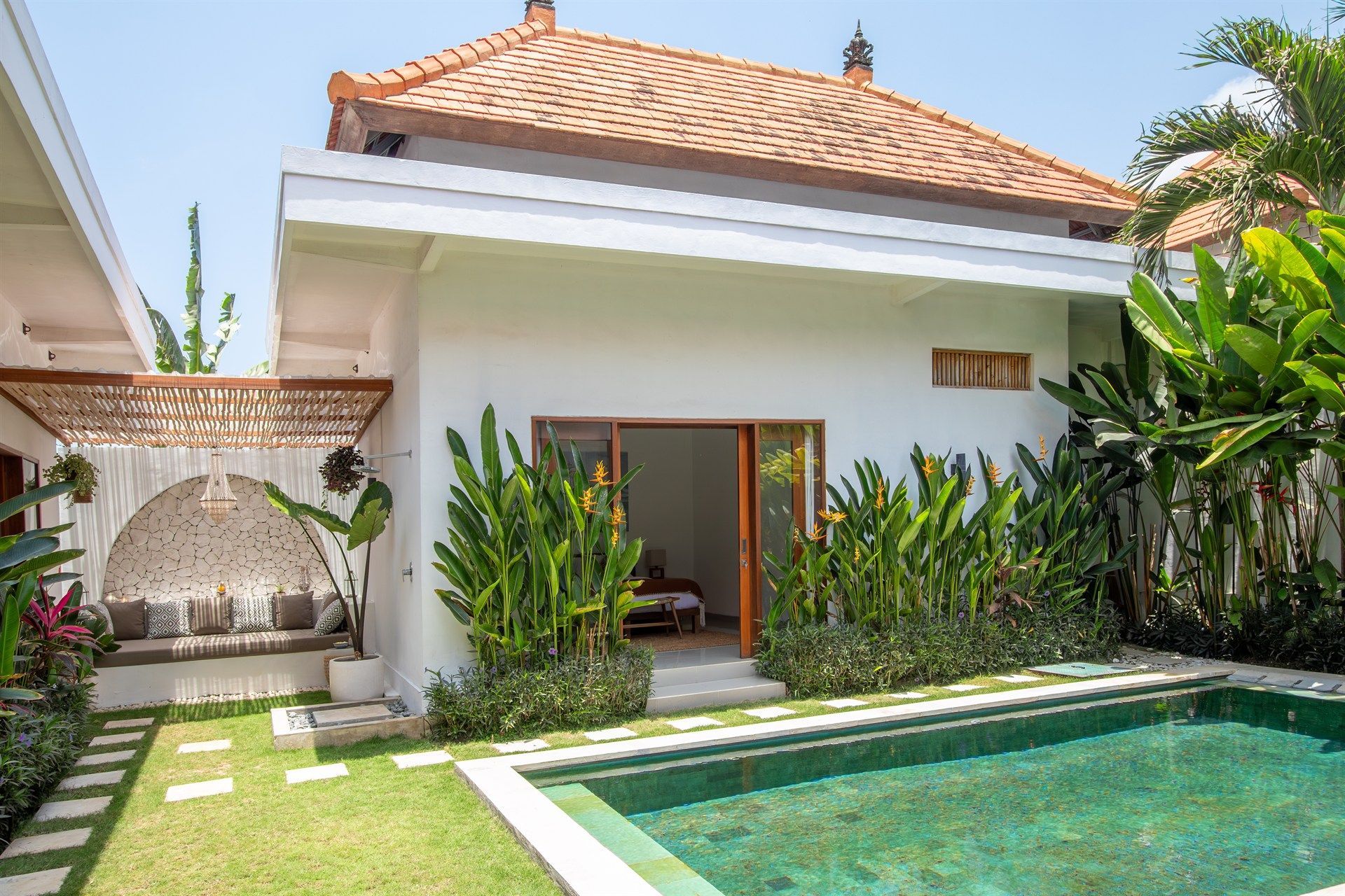 White villa with brown tile roof, sliding doors, and a small pool surrounded by greenery.