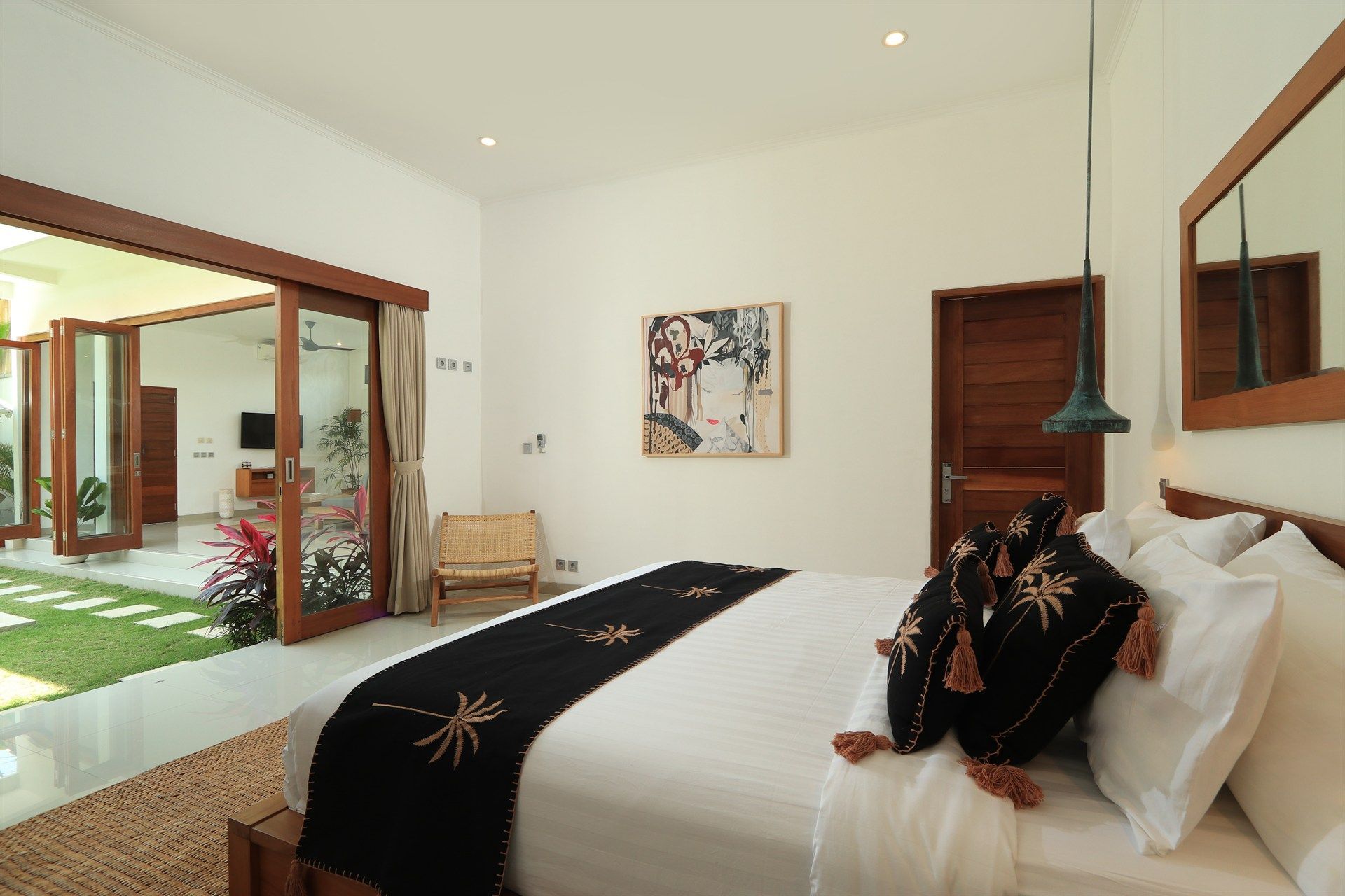 Bedroom with open doors to a patio; white walls, wooden trim, bed with decorative pillows, art.