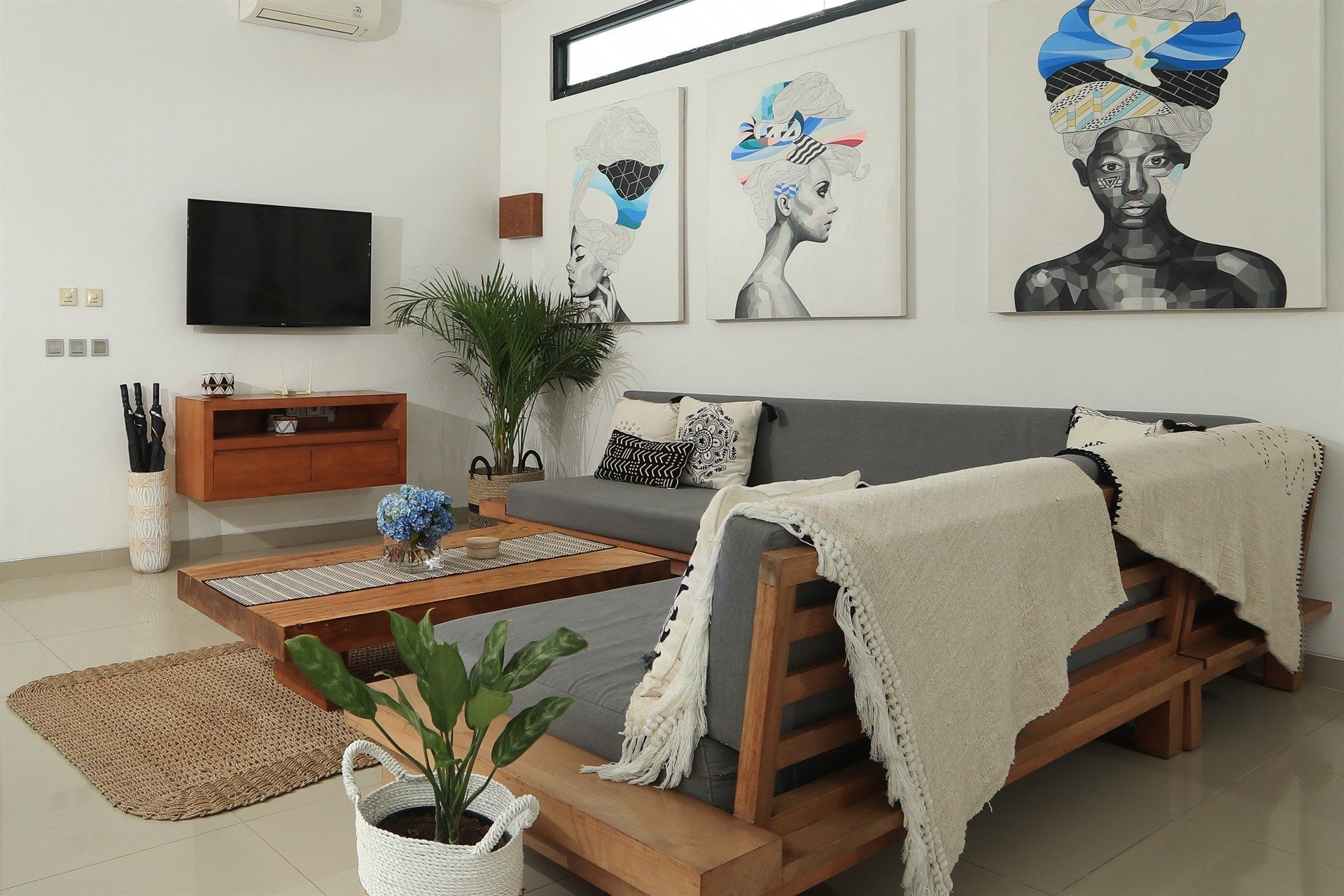 Living room with art, a gray couch, wooden coffee table, and TV on white wall.