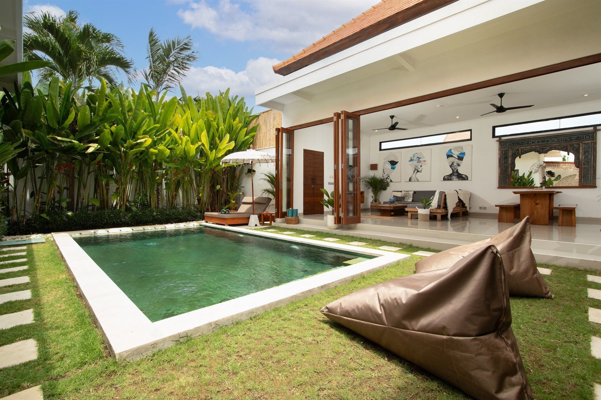 Villa with a pool, garden, and seating area. Brown bean bag chairs on green grass.
