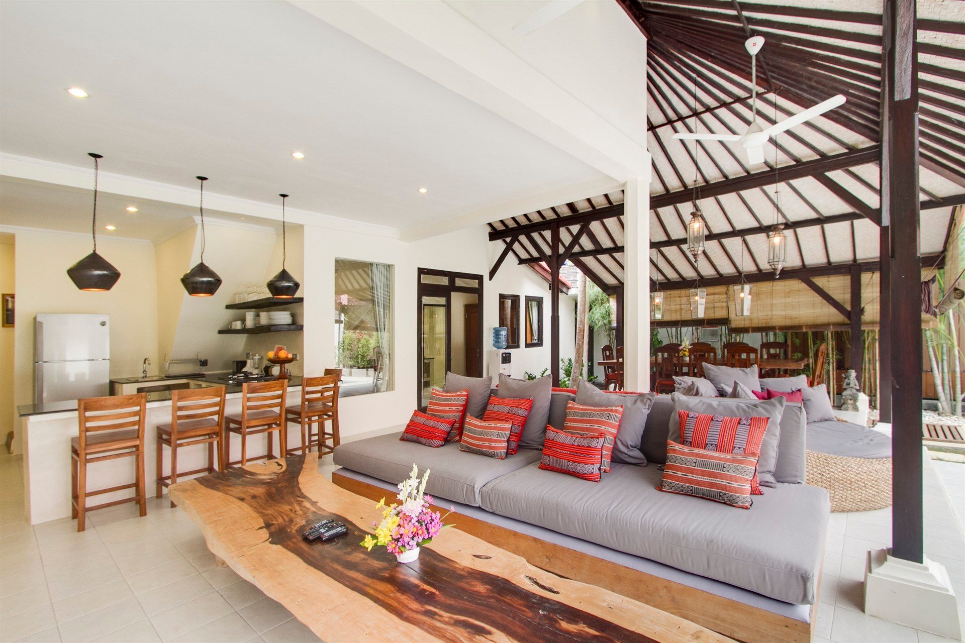 Open-plan living space with kitchen, seating area, and wooden table under a high, wood-beamed ceiling.