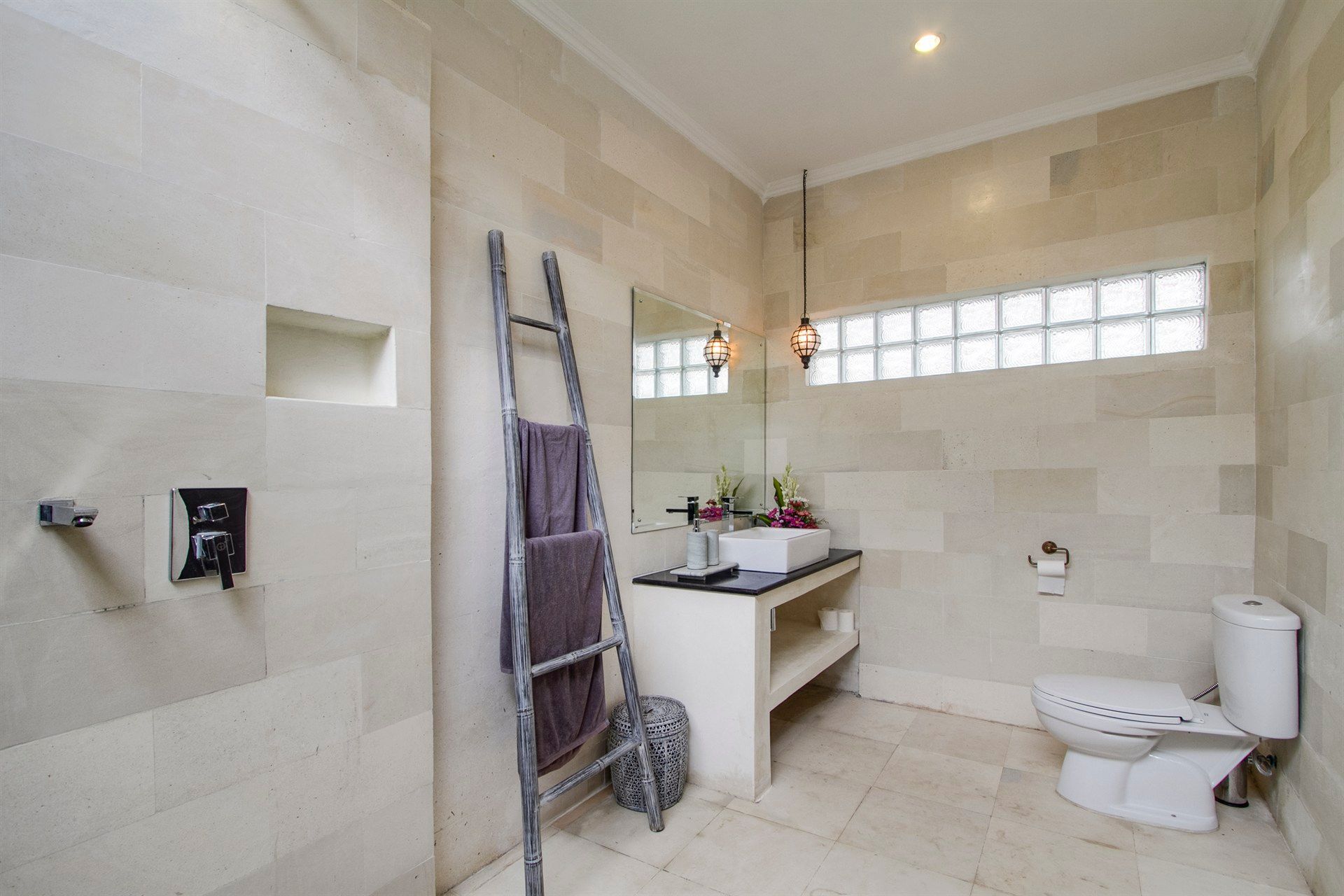 Bathroom with stone walls, ladder with towels, vanity, toilet, and decorative lighting.