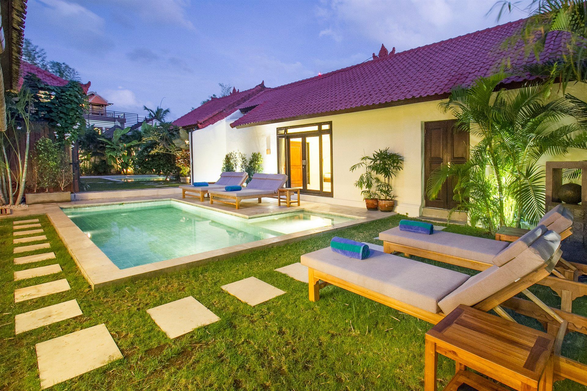 A villa with a pool and lounge chairs on a grassy lawn.