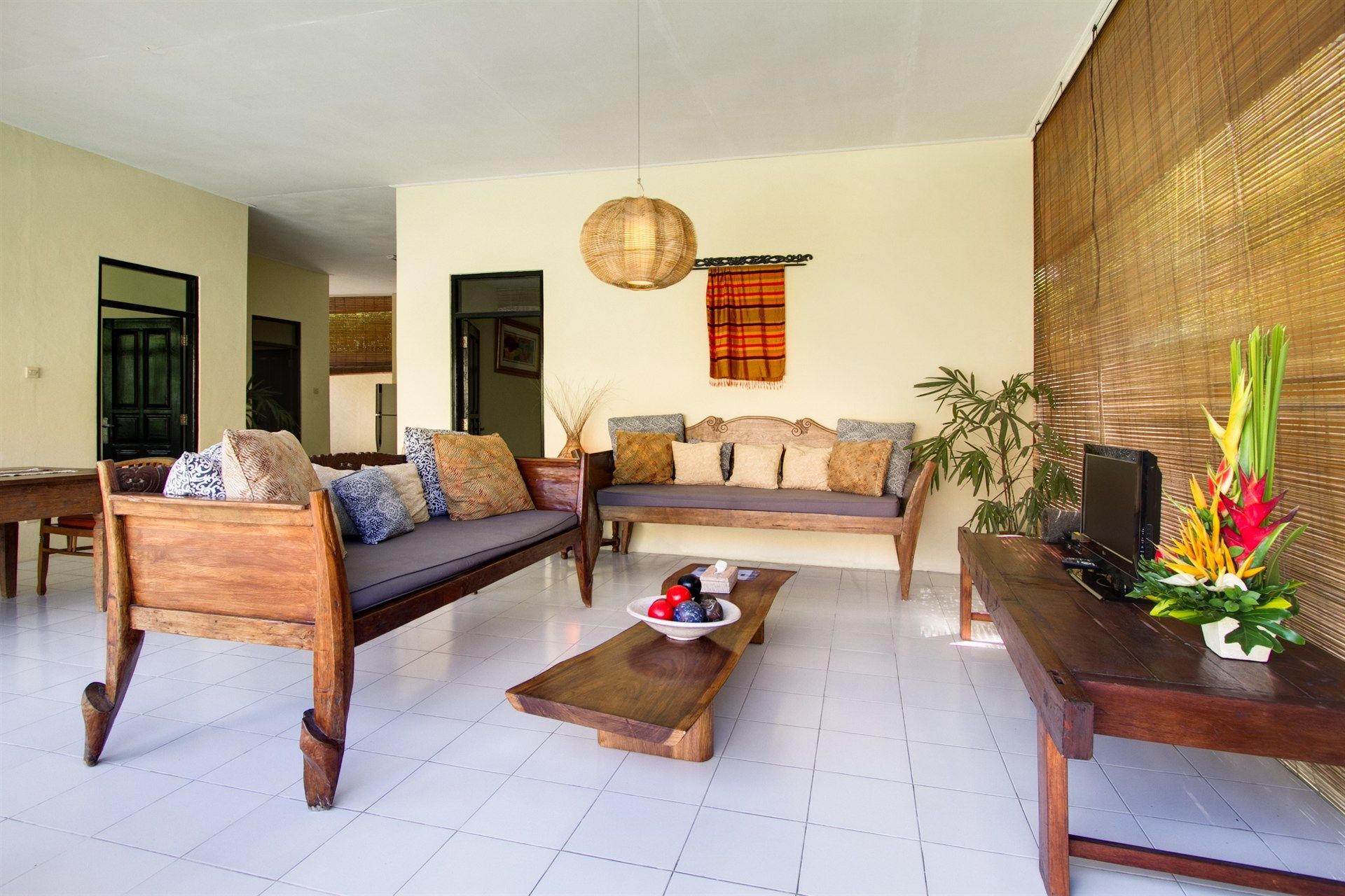 Living room with wooden furniture, including sofas and a coffee table, decorated with cushions and flowers.