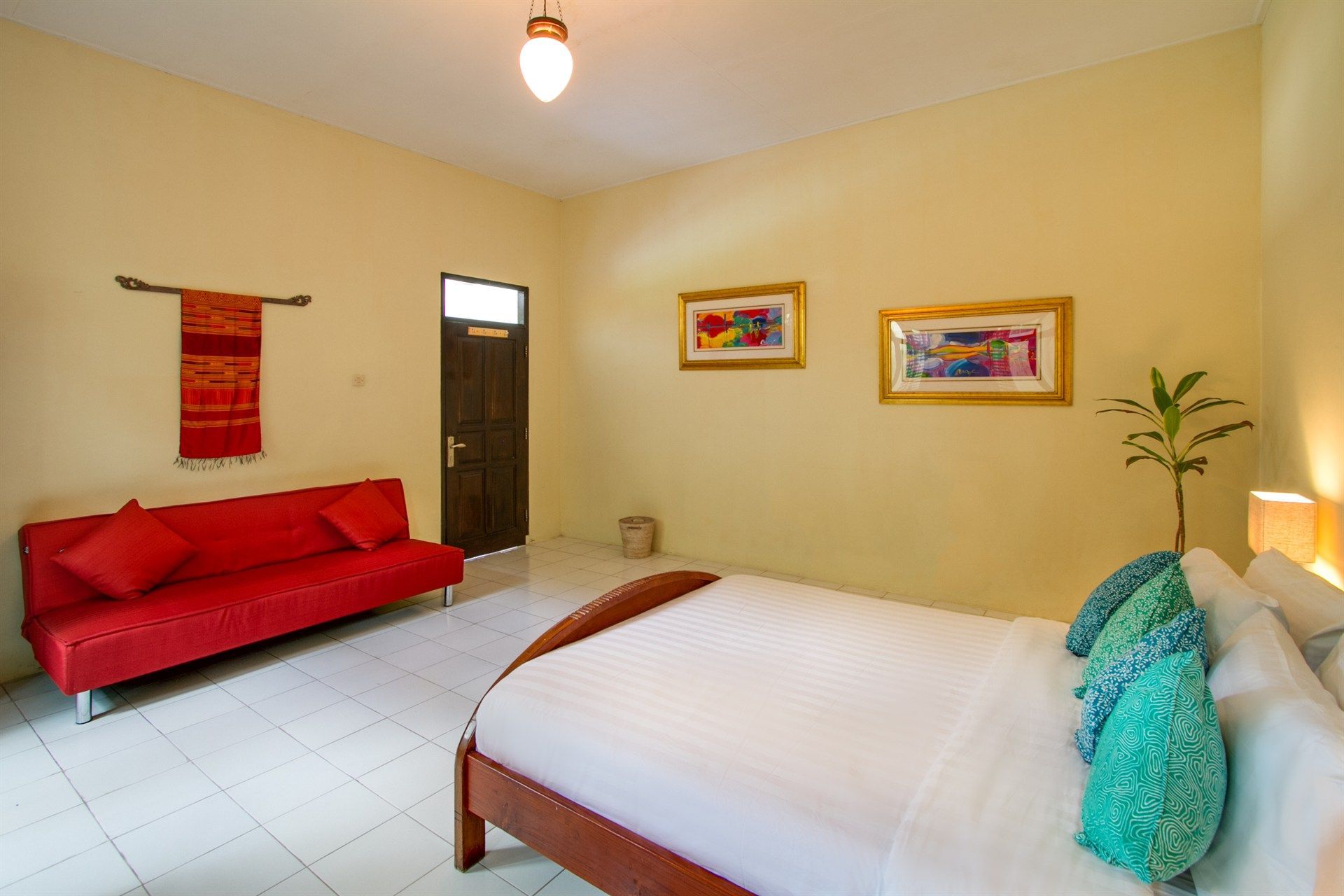 Bedroom with a red sofa, a bed, and framed artwork on yellow walls.