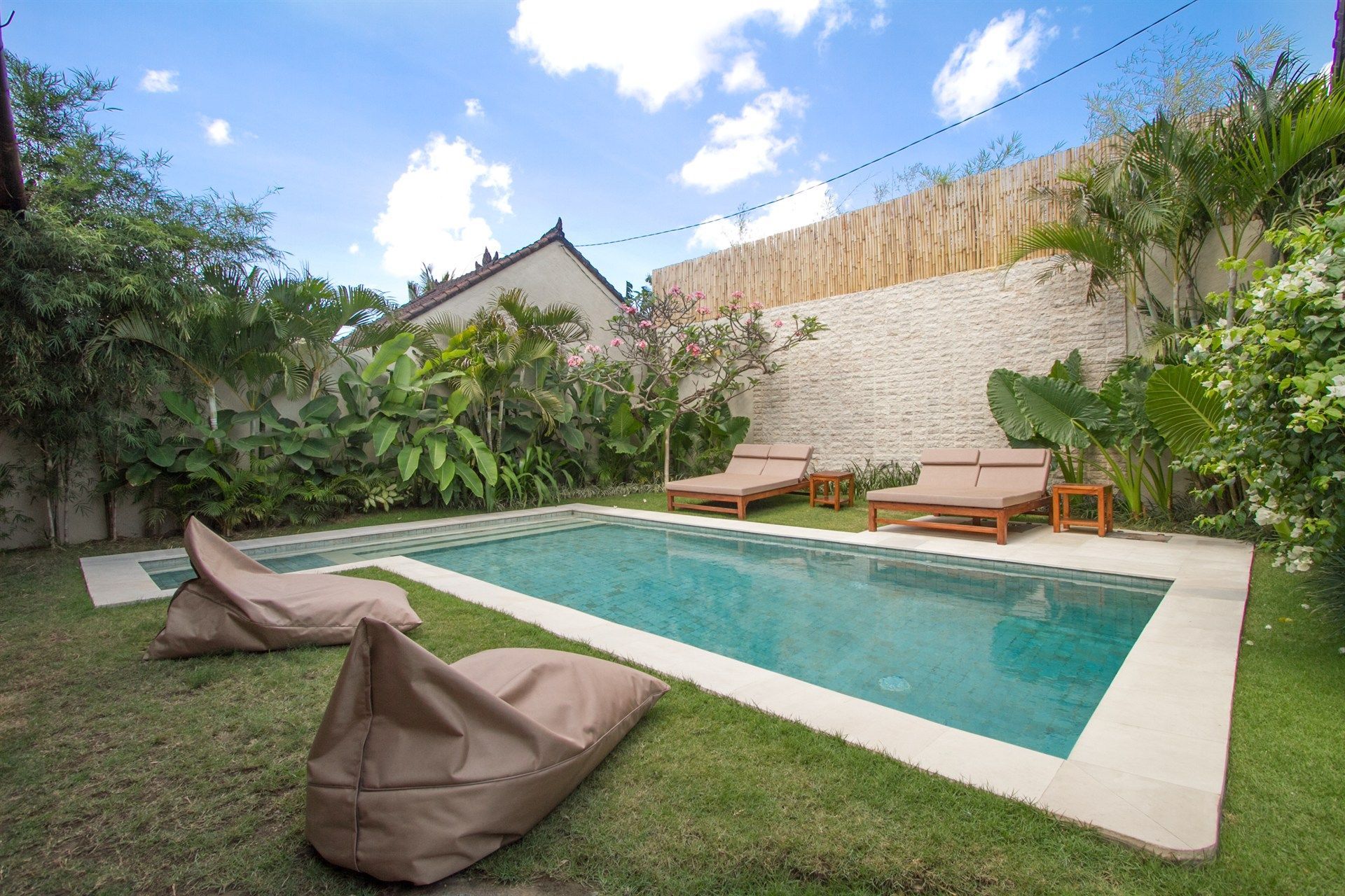 Pool surrounded by lounge chairs and bean bags, in a tropical outdoor setting.