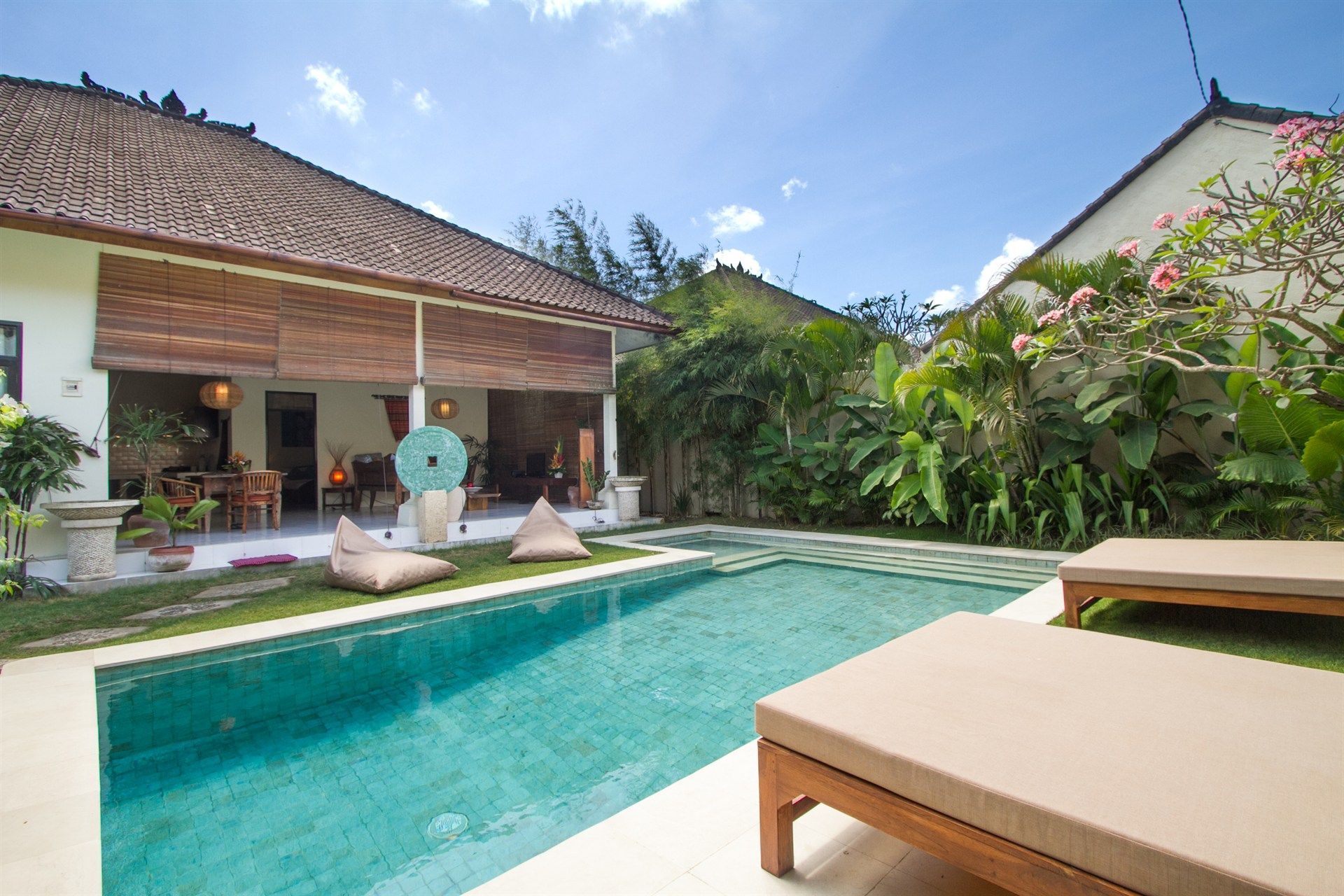 Swimming pool in a tropical garden setting, with lounge chairs, bean bags, and a villa.