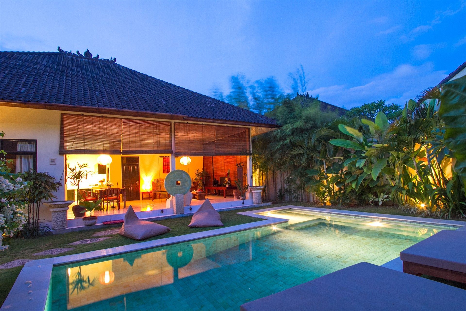 Villa with pool, open to a warm interior with ambient lighting, in a tropical setting at dusk.