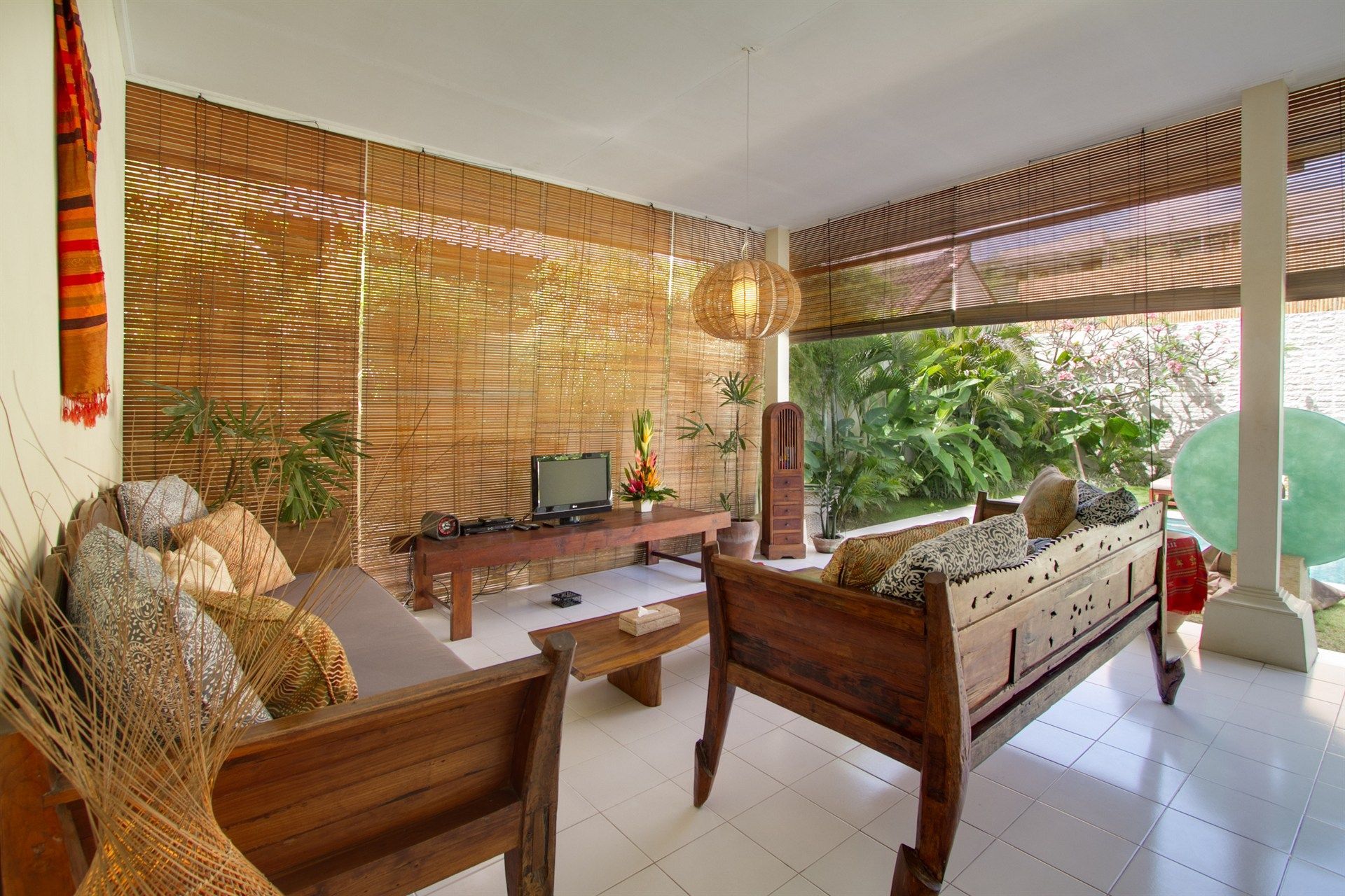 Living room with wooden furniture, woven wall, open to a green garden.