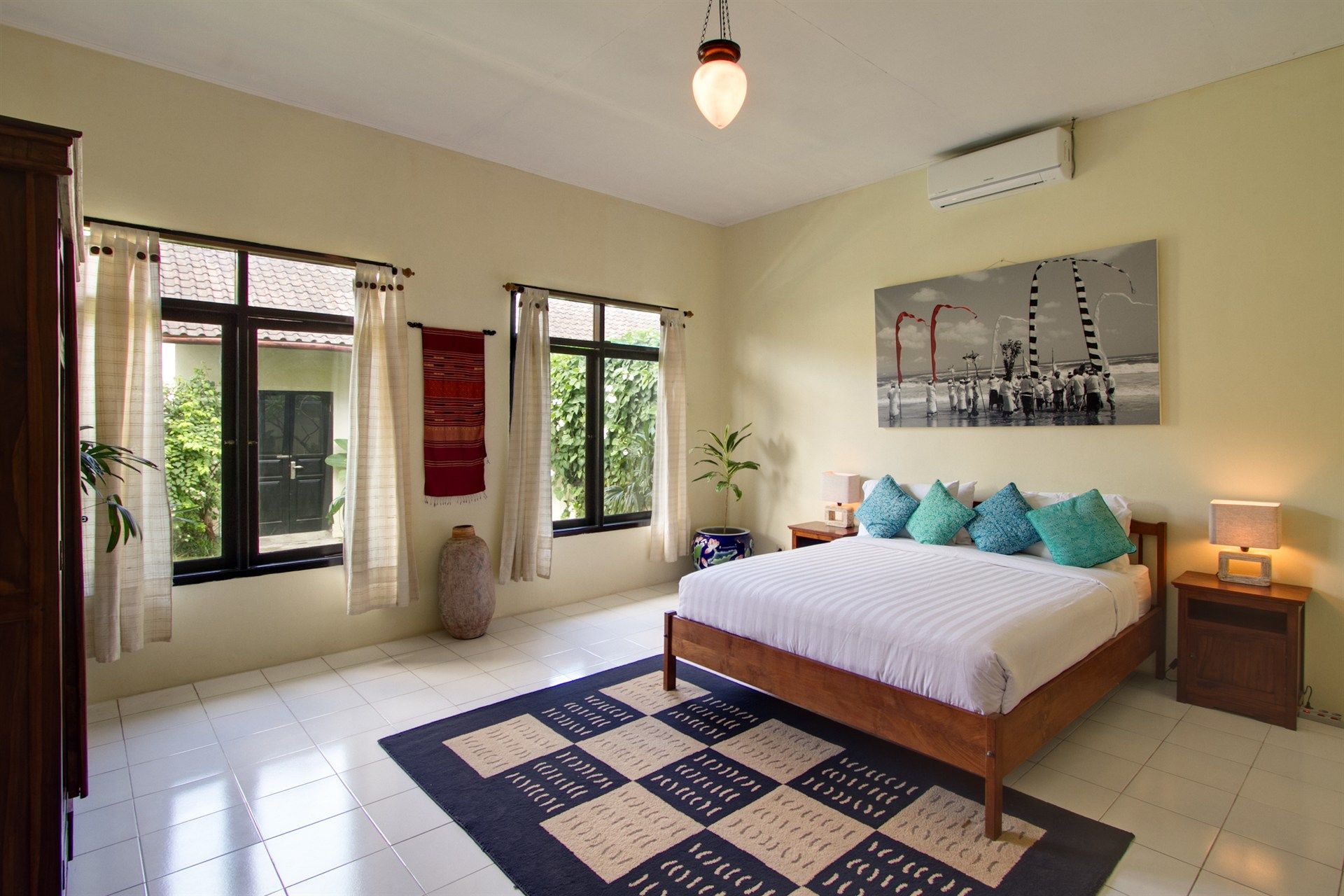 Bedroom with bed, windows, and a large abstract art piece. Blue and white accents on neutral walls.