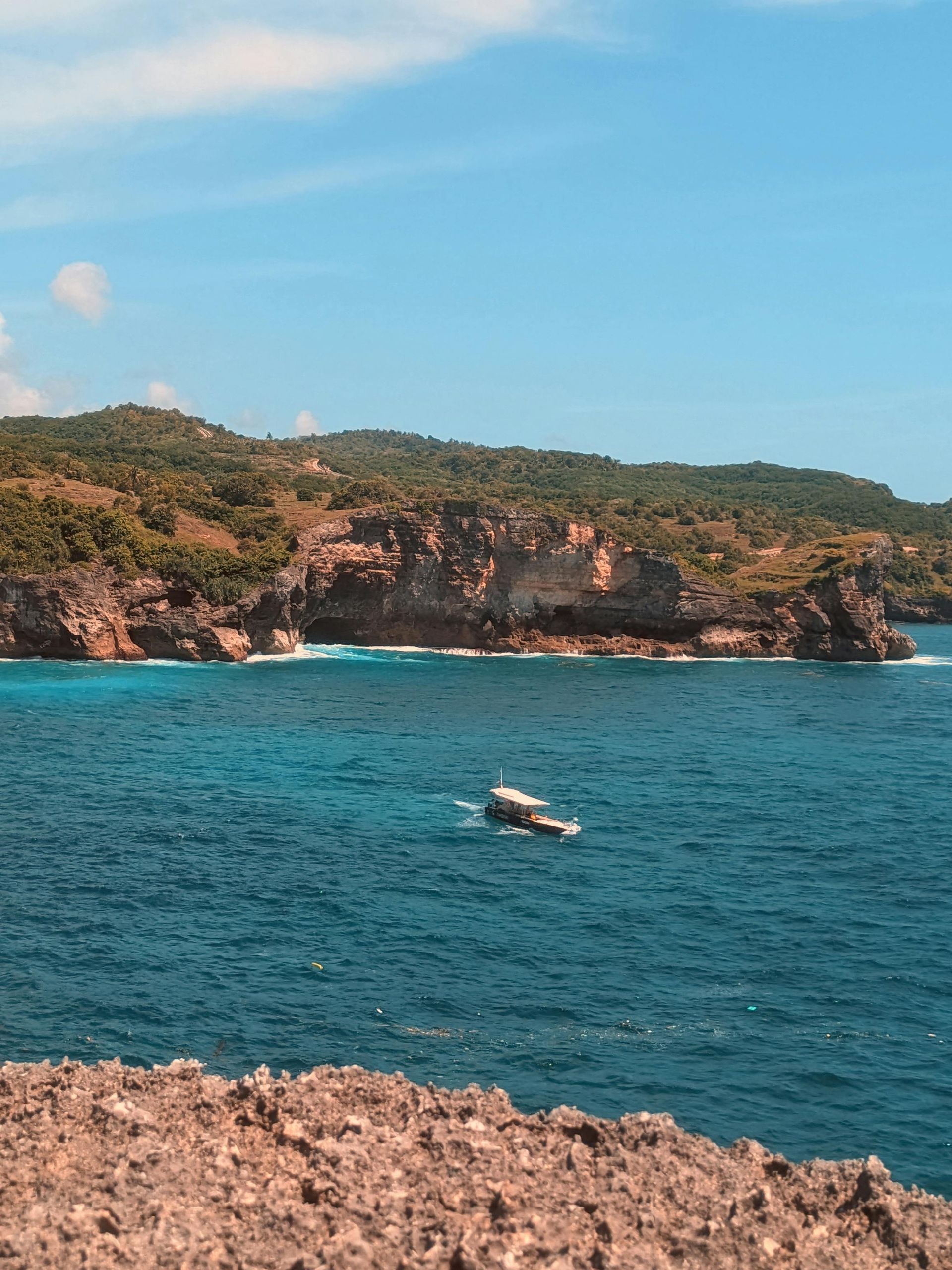 Ocean view with boat near rocky cliffs under a blue sky.