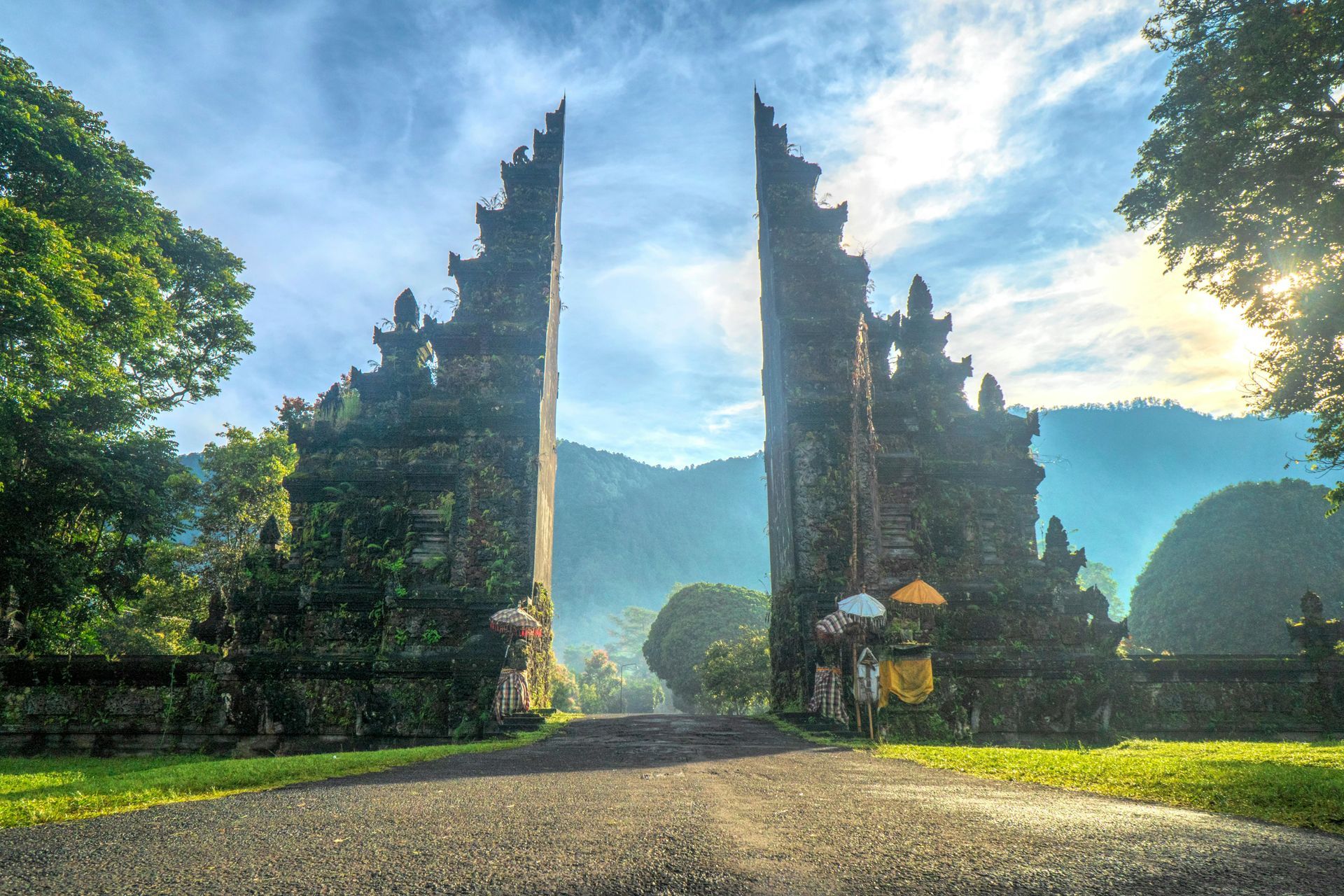 Stone temple gates opening to a misty mountain landscape; two figures with umbrellas stand at the entrance.