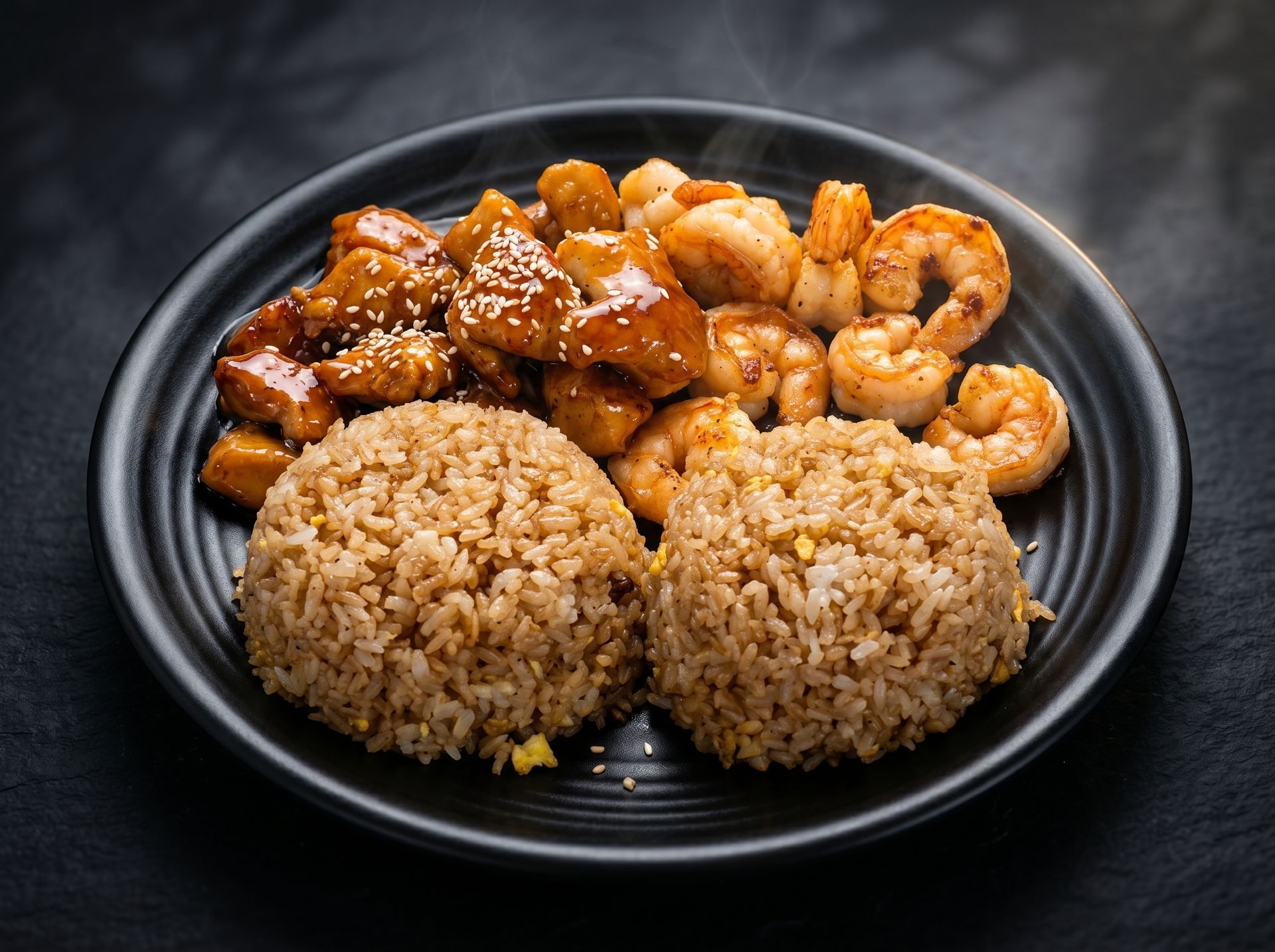 Plate of rice with glazed chicken and shrimp on a dark table