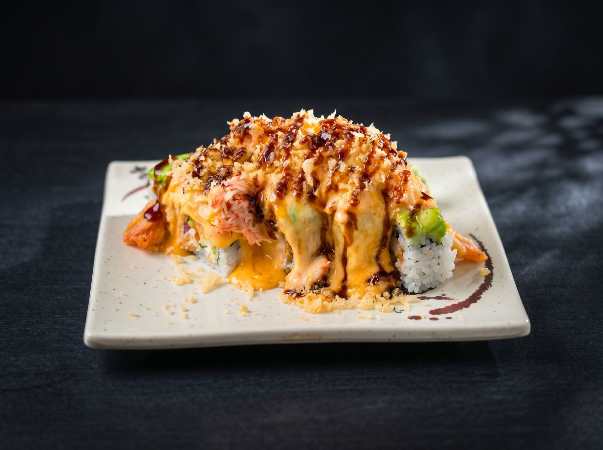 Sushi roll topped with creamy sauce and crispy flakes on a white square plate