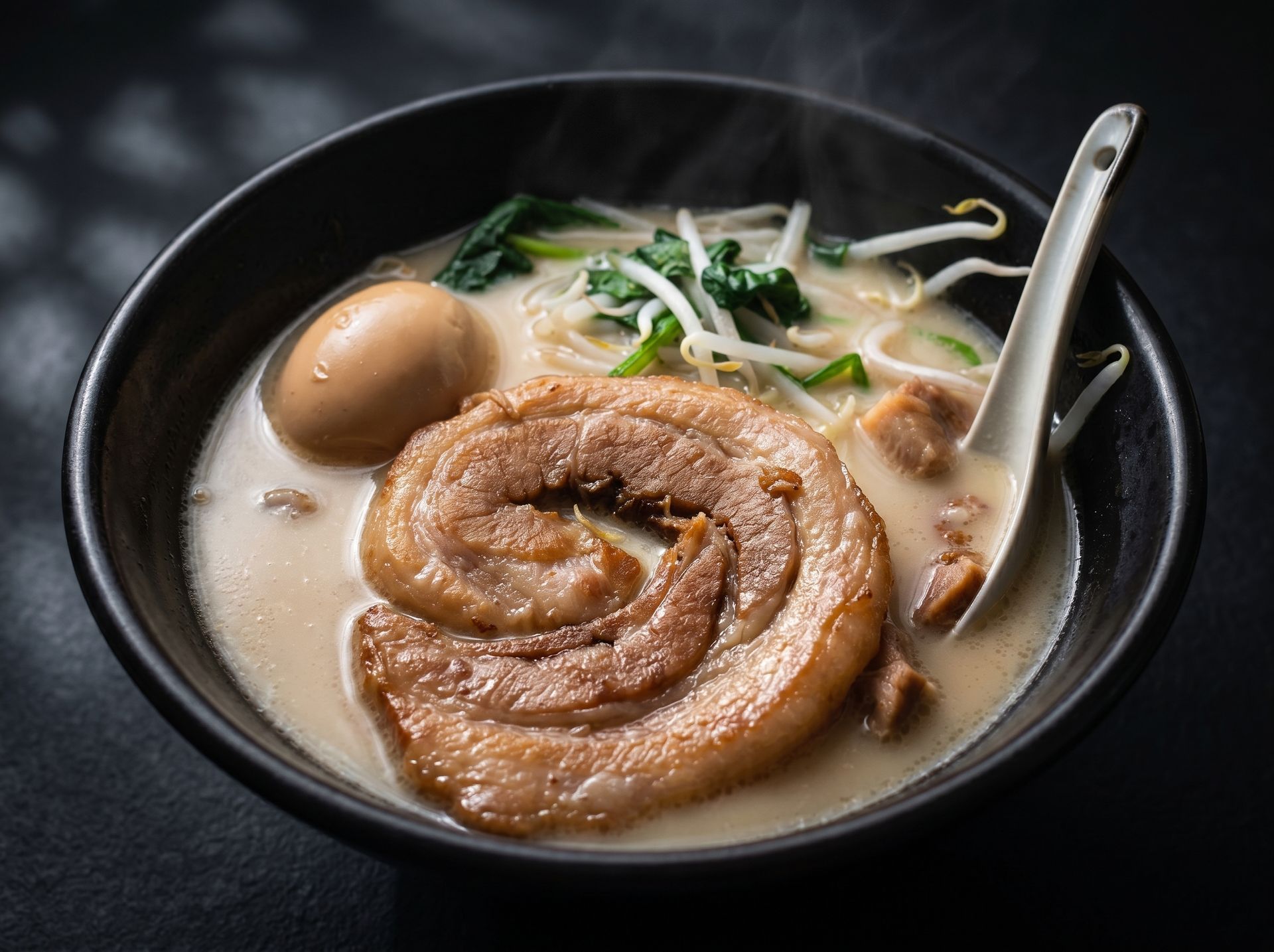 Bowl of creamy noodle soup with braised pork belly, egg, and greens, with a spoon