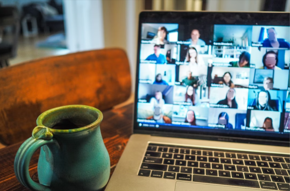 Laptop showing video conference with many participants, beside a turquoise coffee mug.