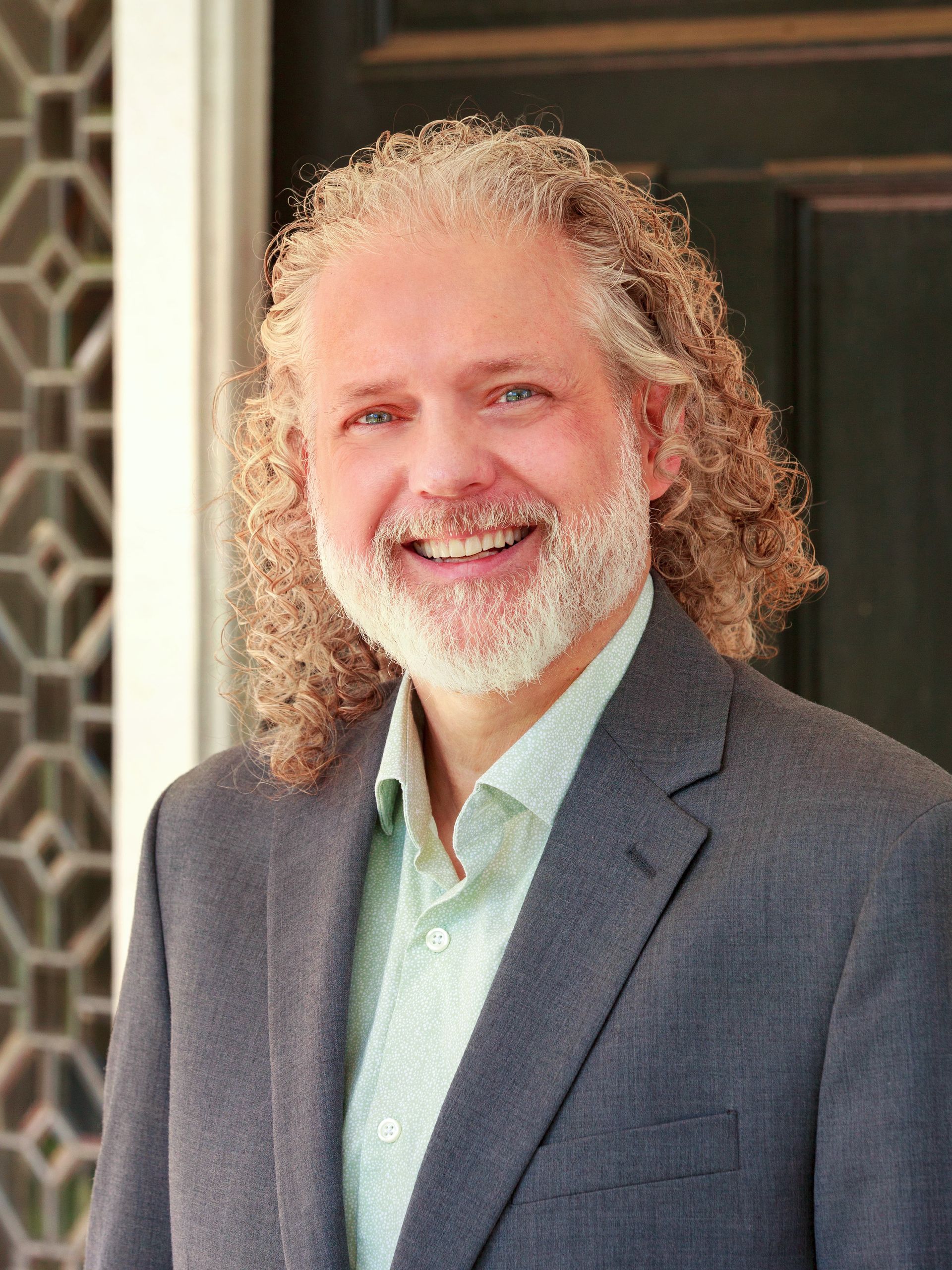 Person with gray curly hair in a red and blue shirt smiles