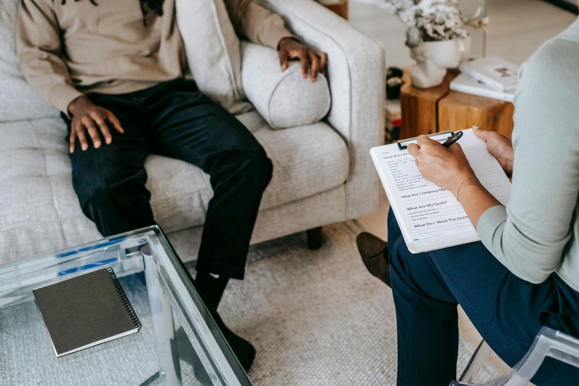 Therapist taking notes during session with a person seated on a couch.
