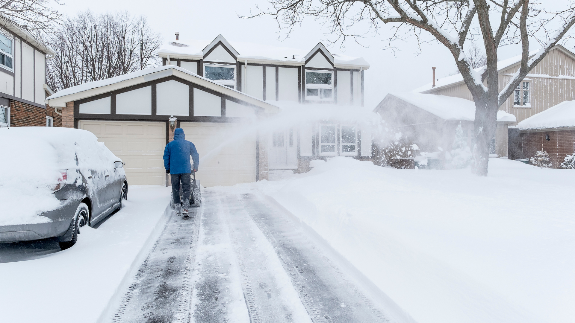 A man is shoveling snow from a driveway in front of a house.