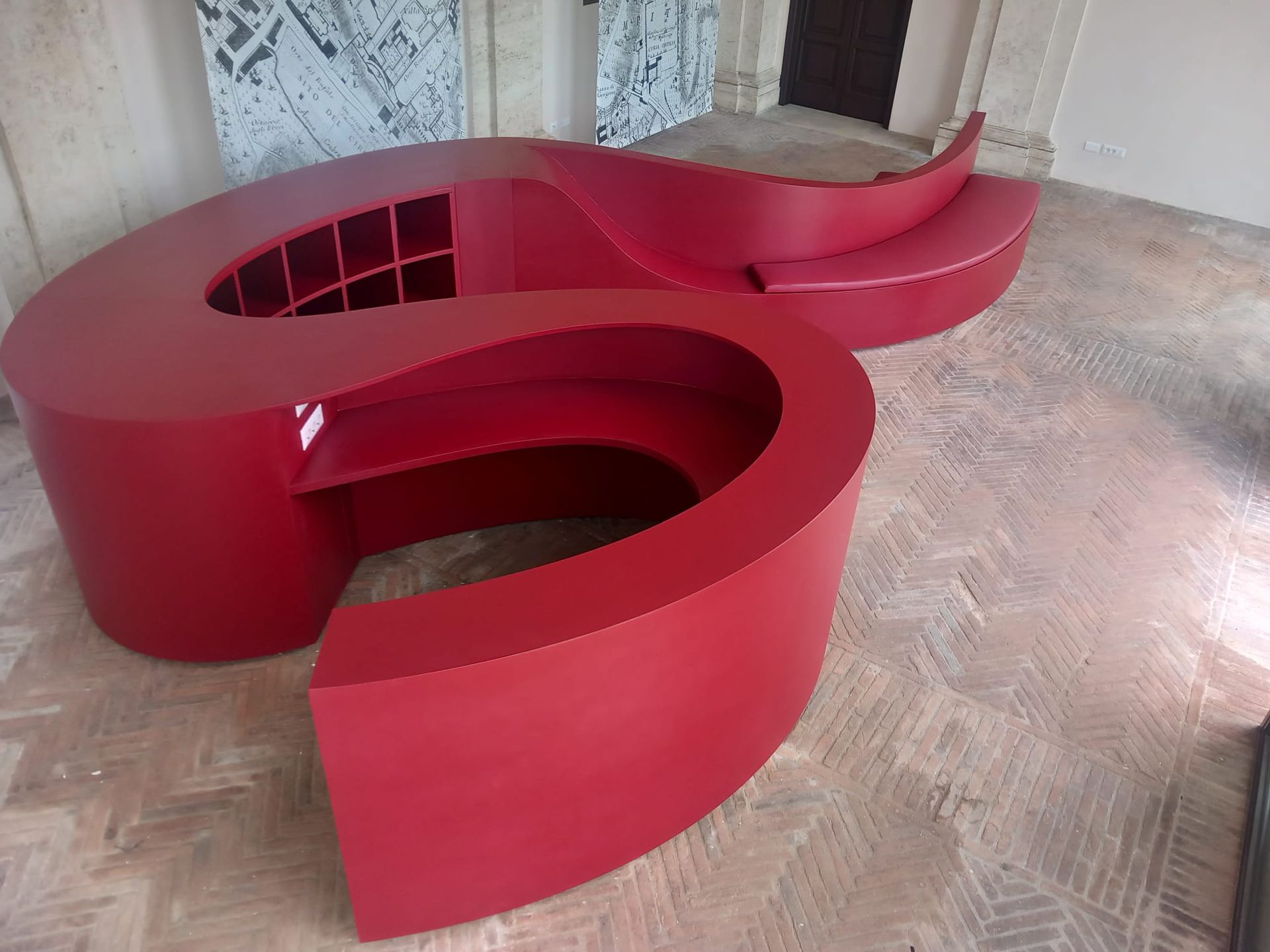 Scrivania o bancone a spirale di colore rosso con ripiani integrati, in un ambiente di officina.