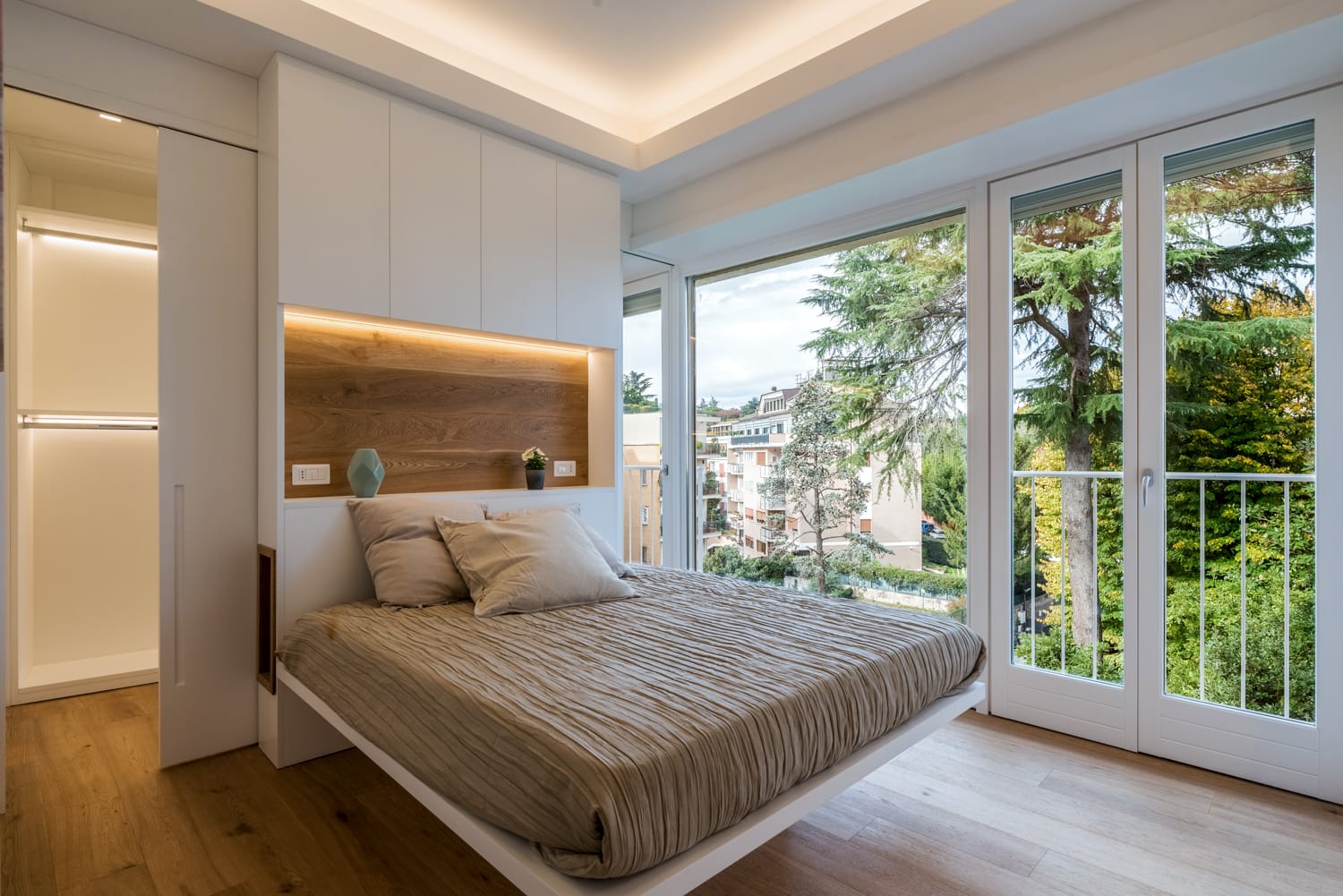 Camera da letto moderna con letto, dettagli in legno e ampie finestre che si affacciano sul verde.