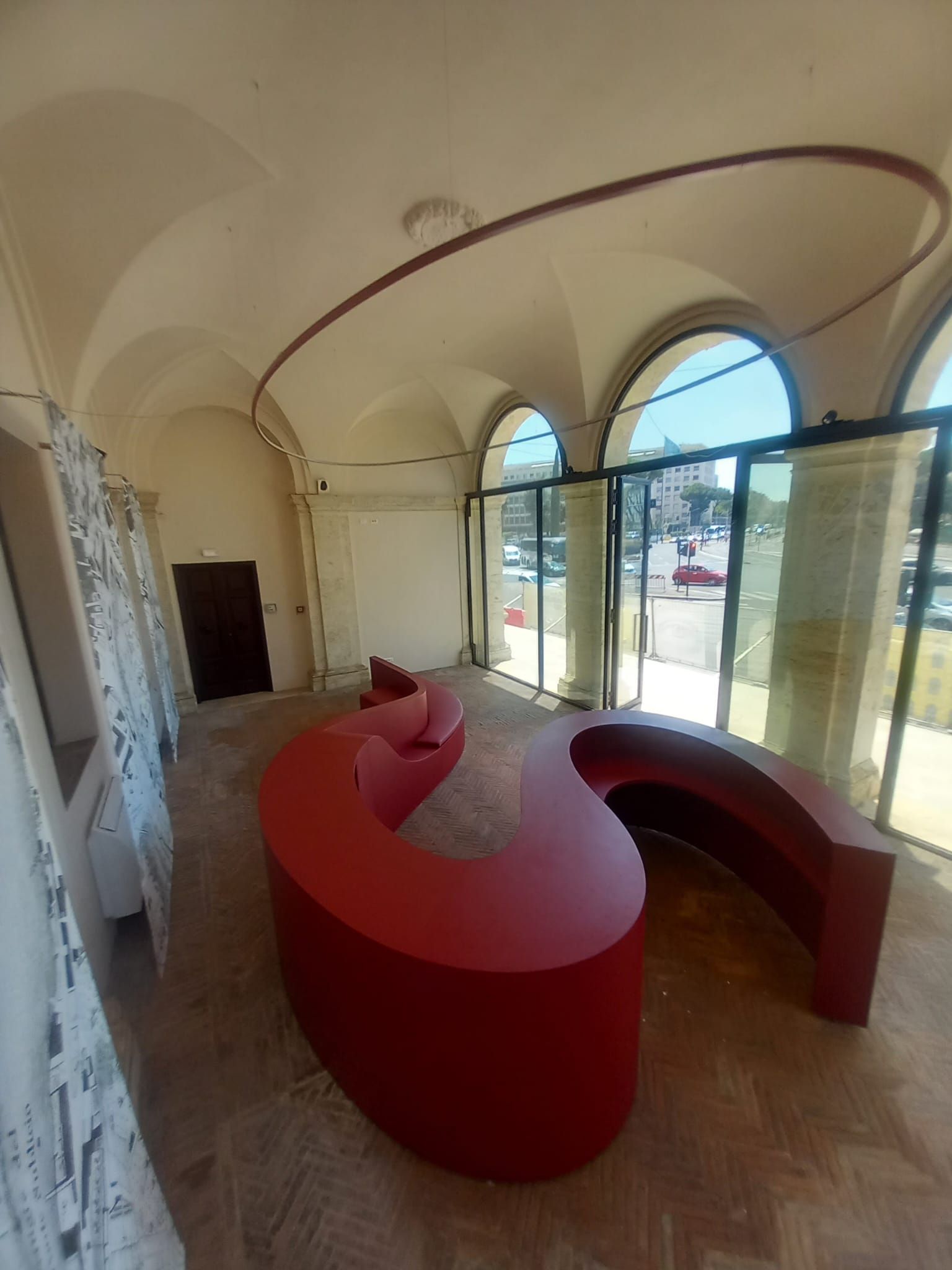 Stanza moderna con panche curve rosse, soffitto a volta e ampie finestre che si affacciano sull'esterno.