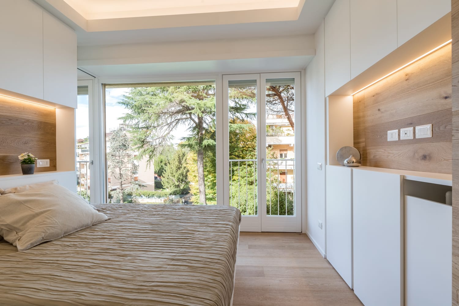 Camera da letto moderna con letto, armadi a muro e porte scorrevoli in vetro che si aprono su una vista sul giardino.