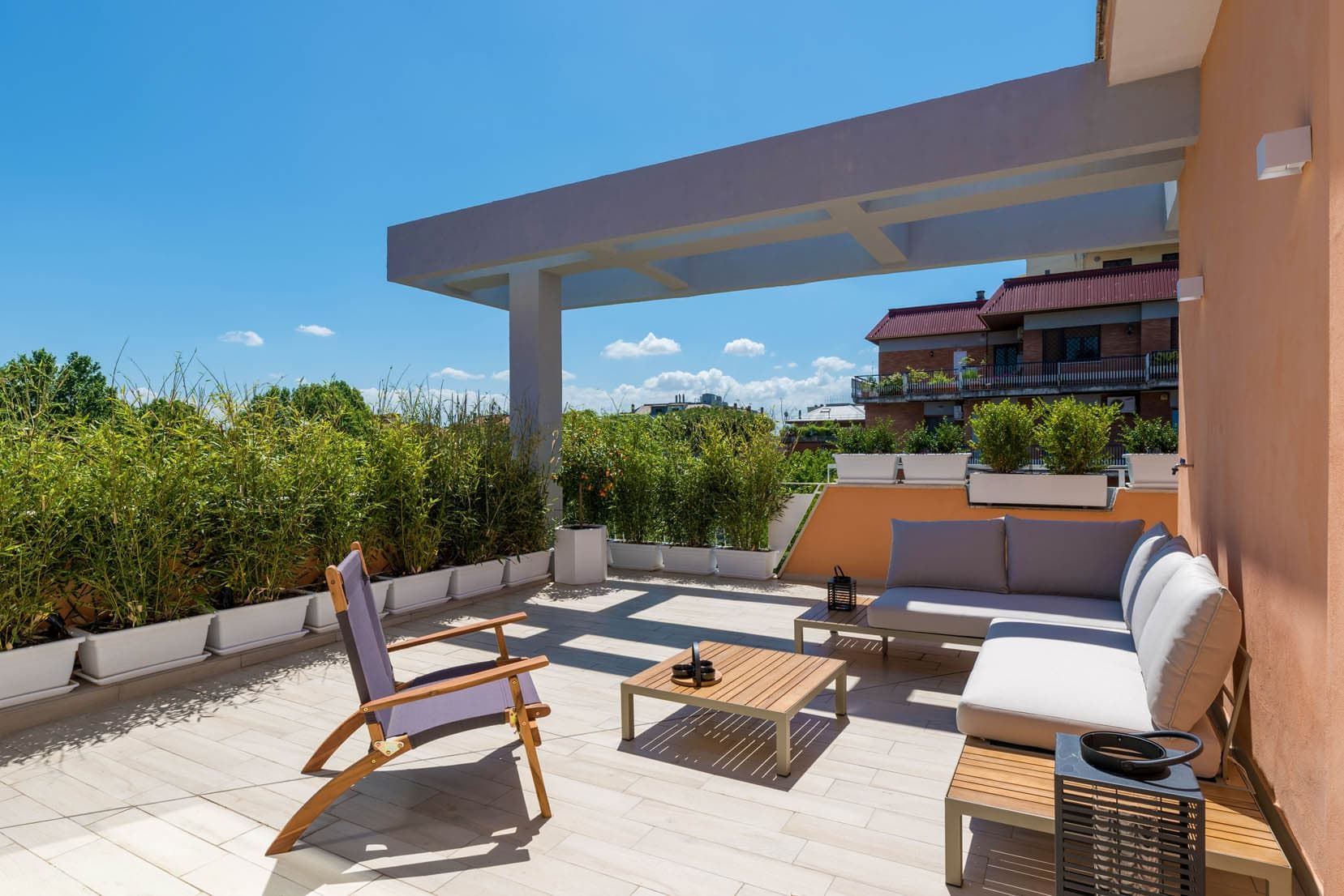 Terrazza panoramica soleggiata con sedute da esterno bianche, sedia in legno e vista sull'oceano.