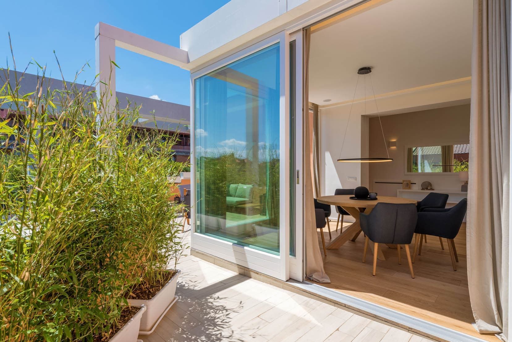 Le porte scorrevoli in vetro si aprono su un luminoso patio con zona pranzo, completa di tavolo e sedie.