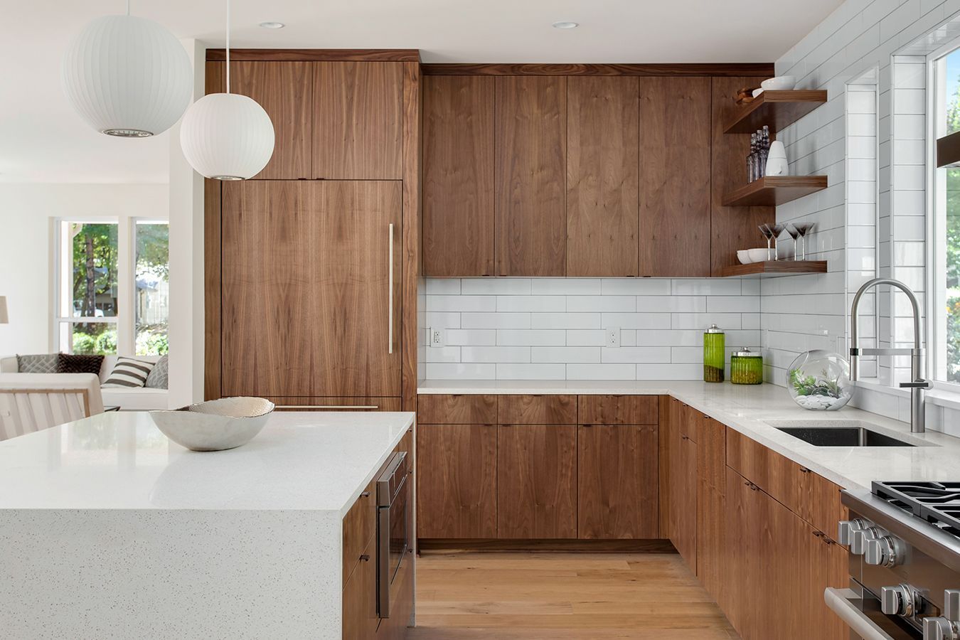 Cucina moderna con mobili in legno, isola bianca, ripiani in marmo e lampade a sospensione.