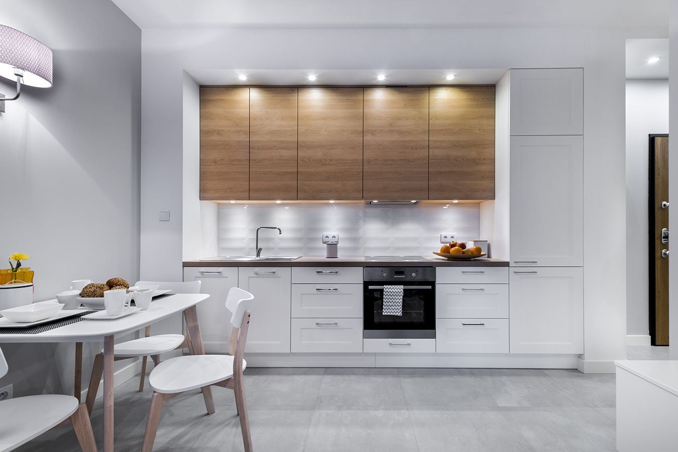 Cucina moderna bianca con mobili in legno, forno a incasso e tavolo da pranzo con stoviglie.
