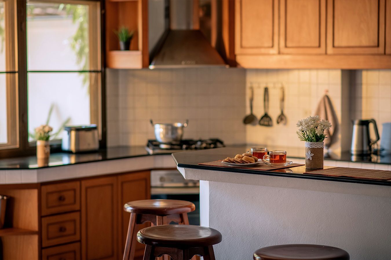Cucina accogliente in legno con isola, sgabelli e luce naturale proveniente da una finestra.