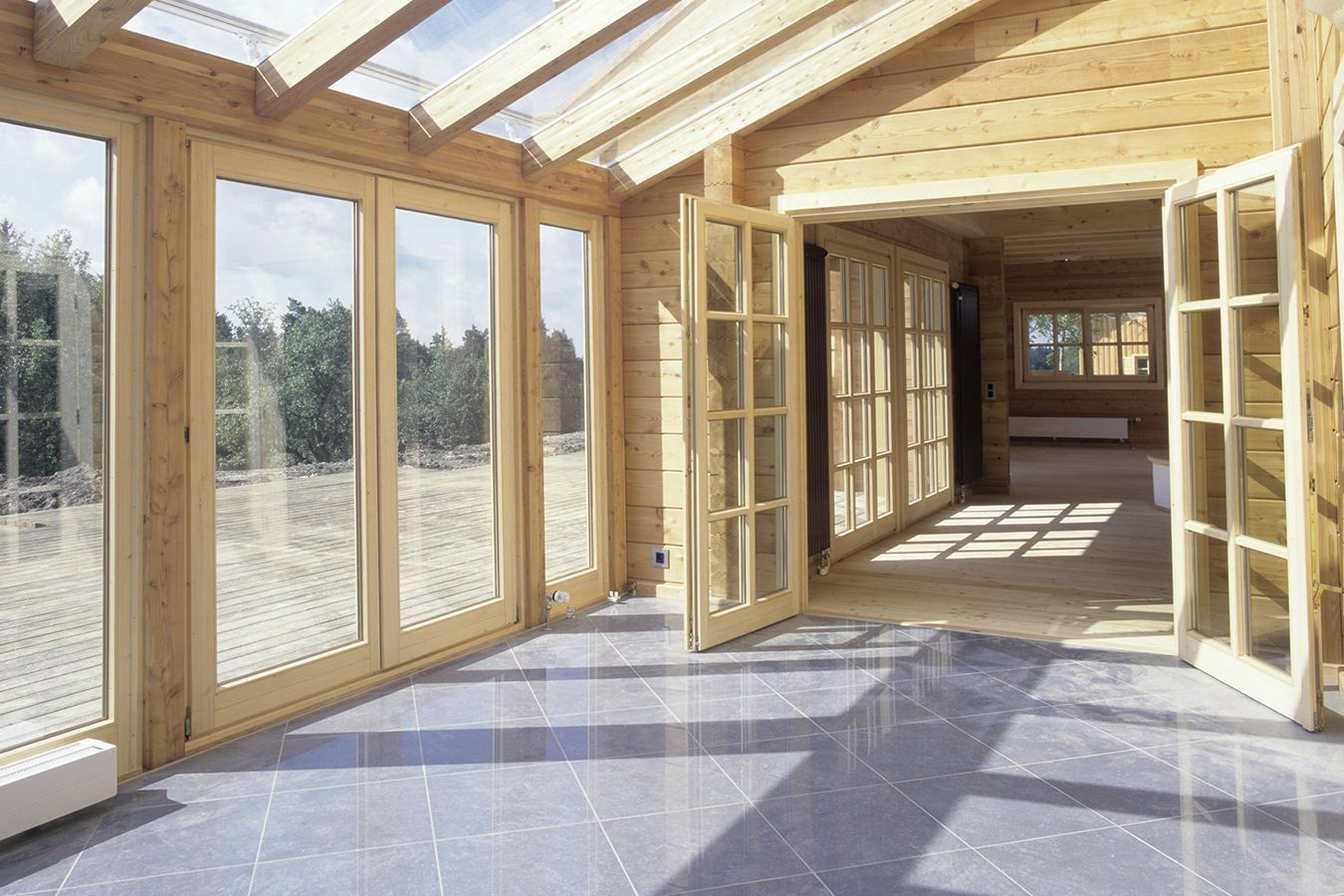 Luminosa stanza in legno con ampie porte e finestre in vetro che si aprono su una veranda coperta.