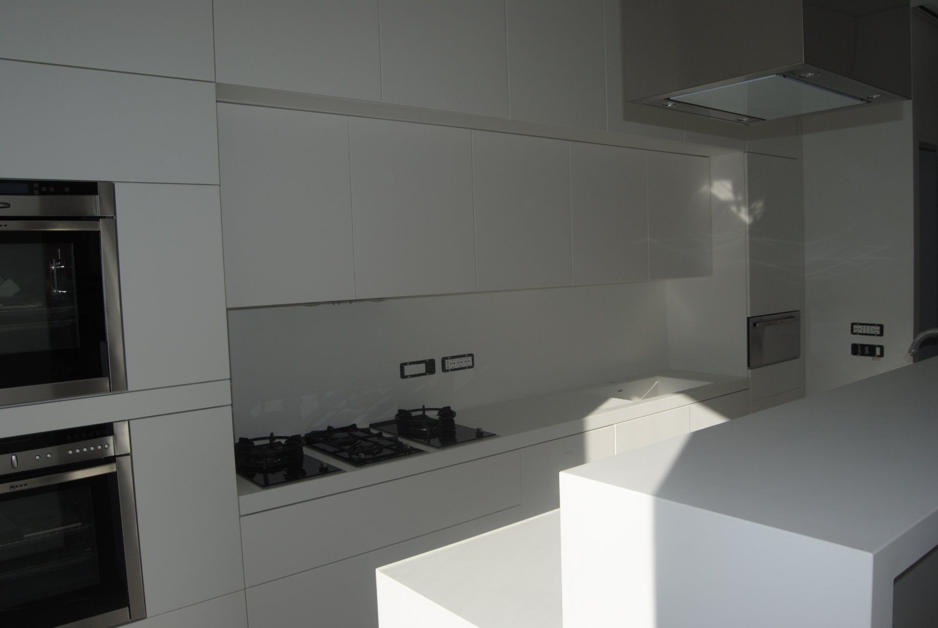 Cucina moderna bianca con forno a incasso, piano cottura e grande isola centrale.