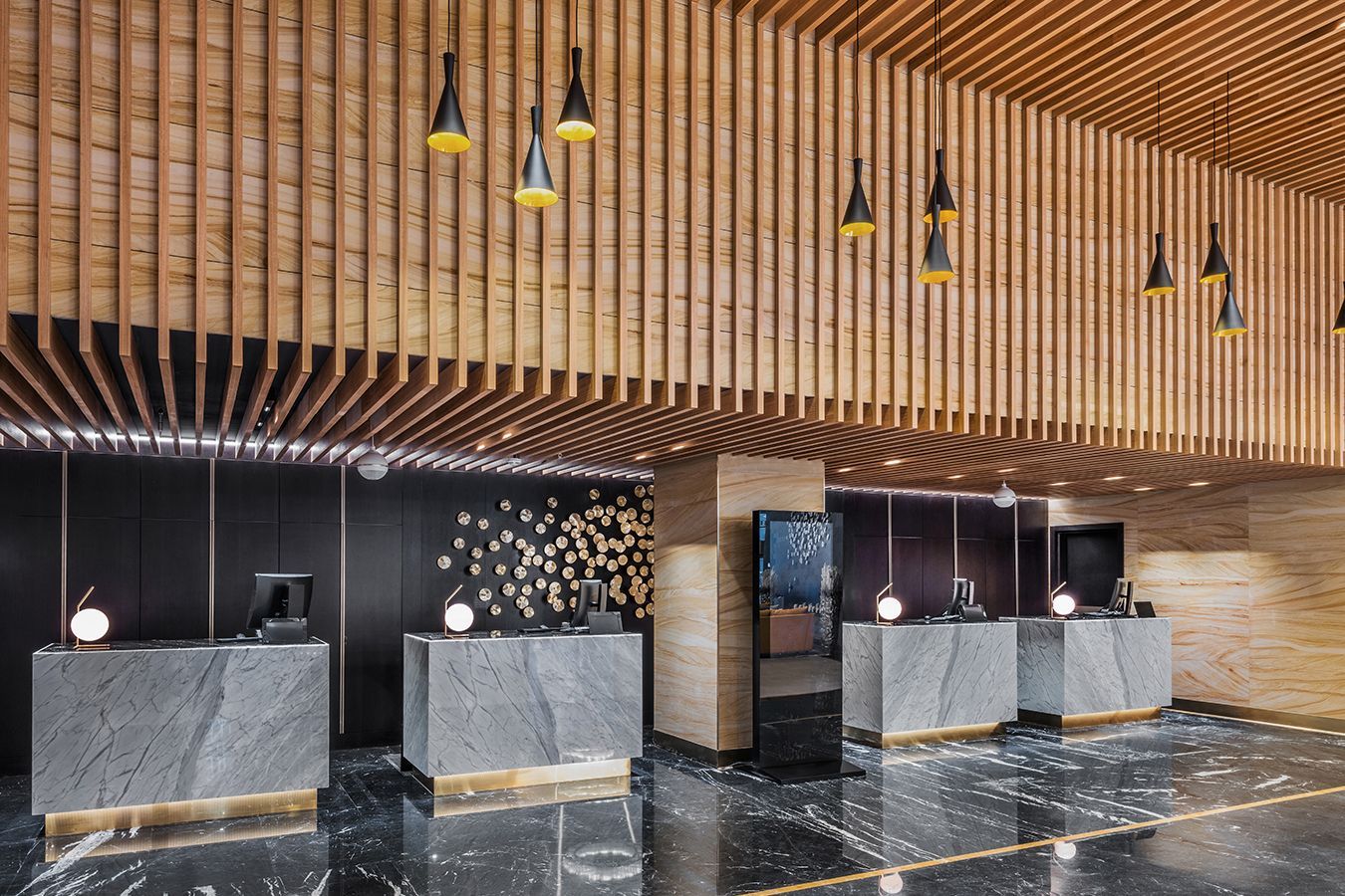 Hall d'albergo moderna con banconi del check-in in marmo, soffitto a doghe di legno, lampade a sospensione e pavimento nero lucido.