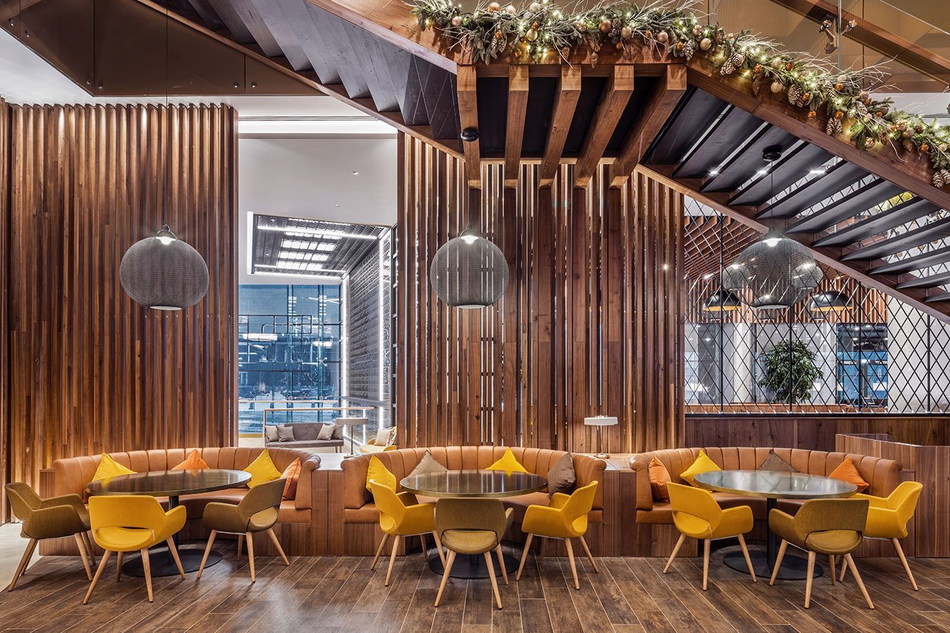 Interni moderni di un ristorante con sedie color senape, pareti a doghe di legno, lampade a sospensione e decorazioni con piante.