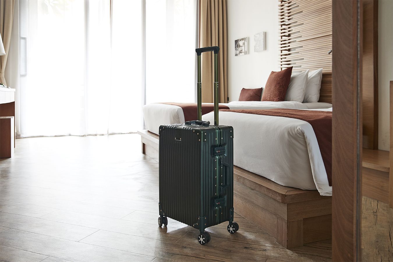 Una valigia verde accanto al letto in una luminosa camera d'albergo.