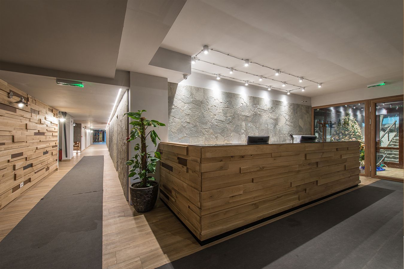 Hall d'ingresso moderna per uffici con bancone reception in legno, parete in pietra, corridoio e pianta in vaso.