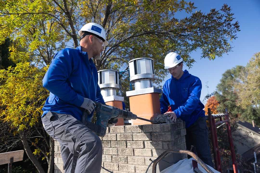 A guardian chimney solutions technician wearing a hard hat and safety vest is working on a chimney on top of a roof.