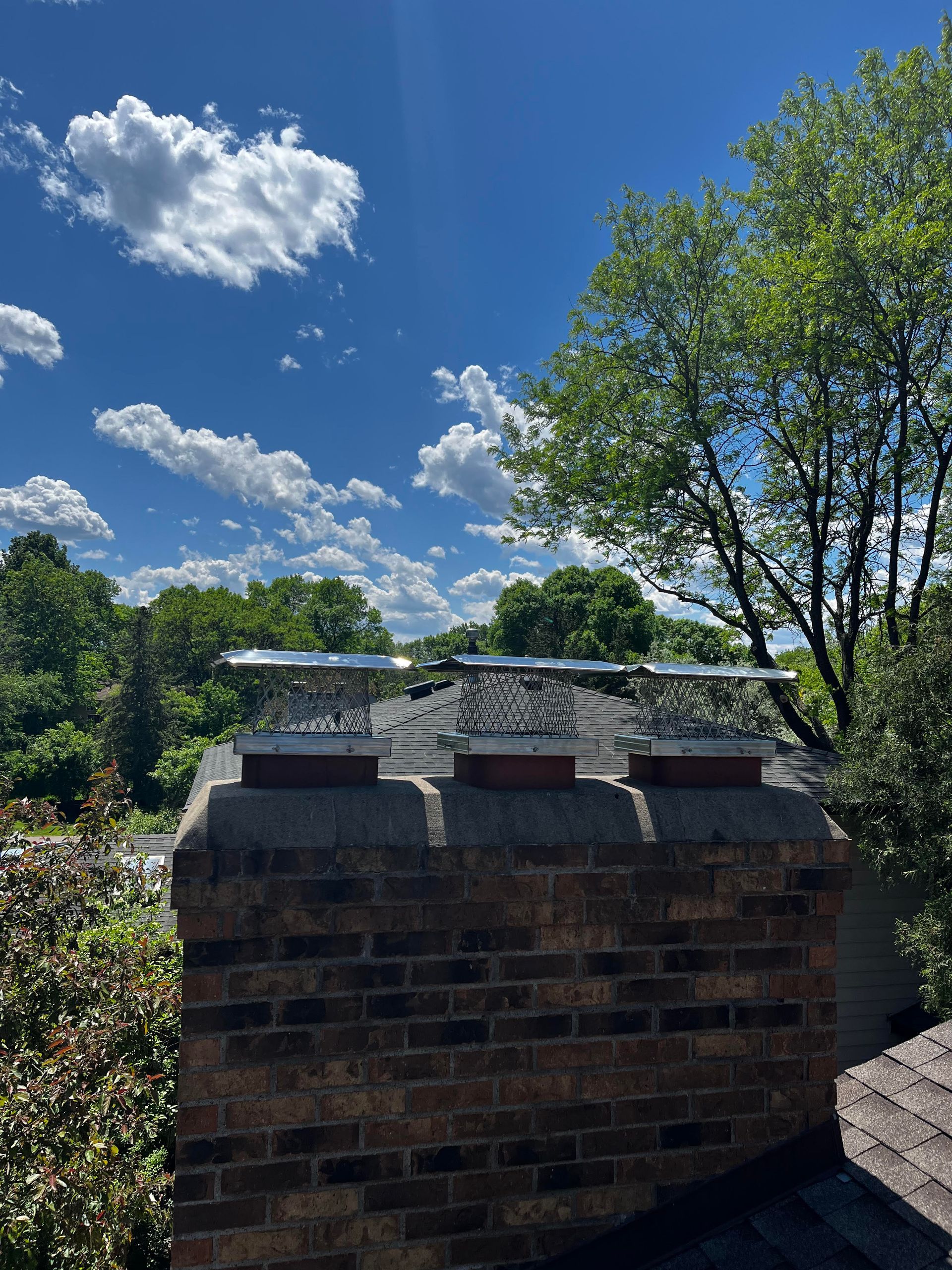 A brick chimney on top of a roof with trees in the background