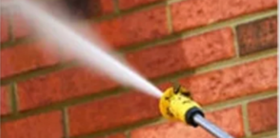 A high pressure washer is spraying water on a brick wall.