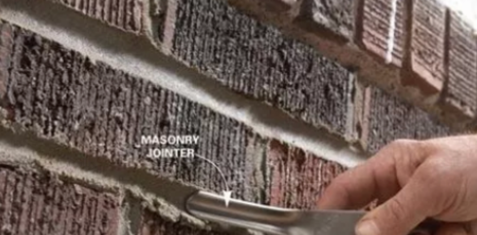 A person is holding a wrench in front of a brick wall.
