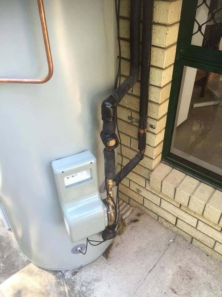 A Water Heater is Attached to the Side of a Brick Building — Reed Plumbing Industries in Mackay, QLD